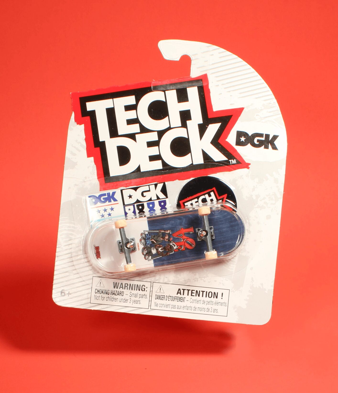 Packaging for a Tech Deck fingerboard set with a transparent case and small accessories inside, on a red background.
