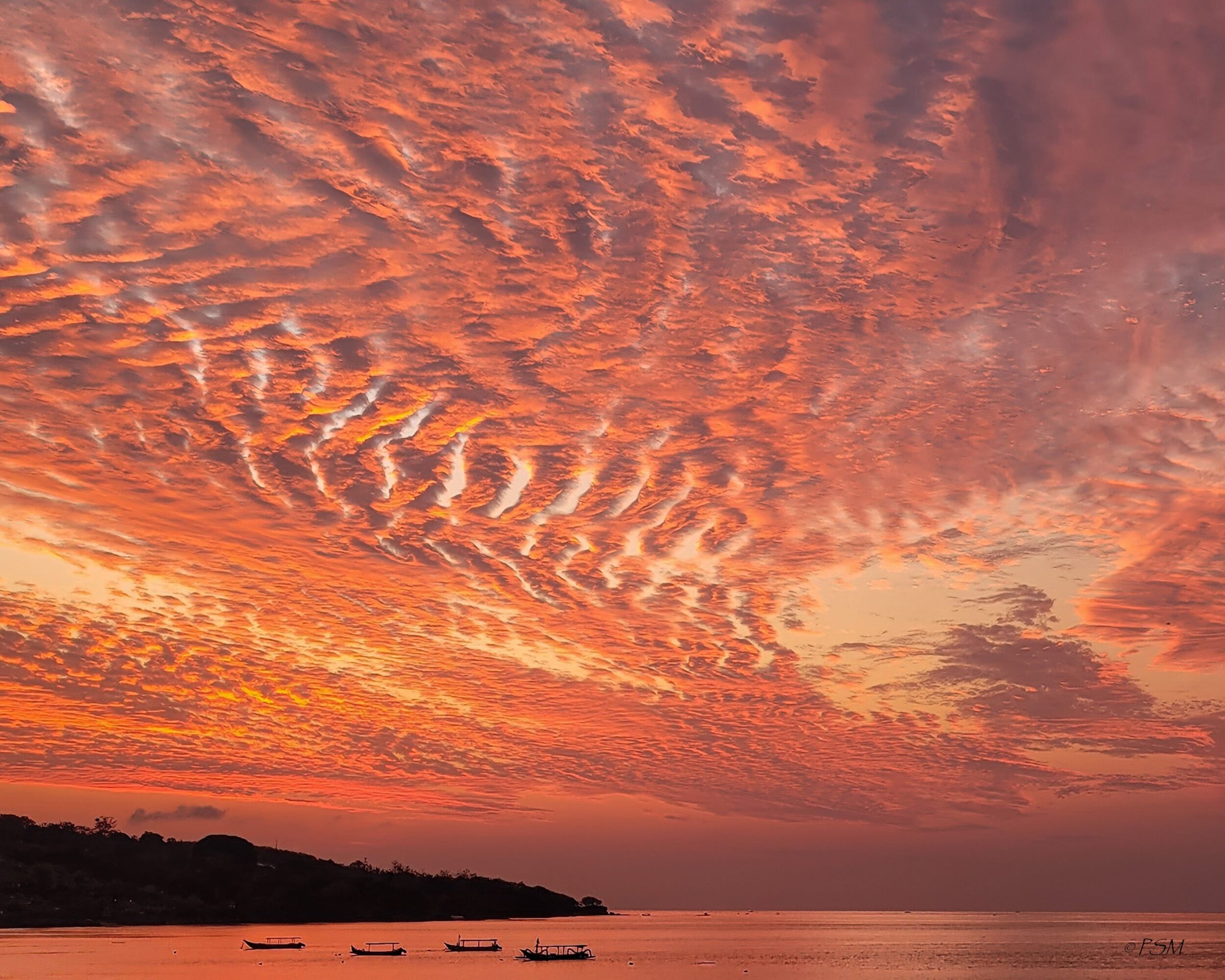 Colorful sunset sky with textured clouds over a calm body of water and a distant shoreline.