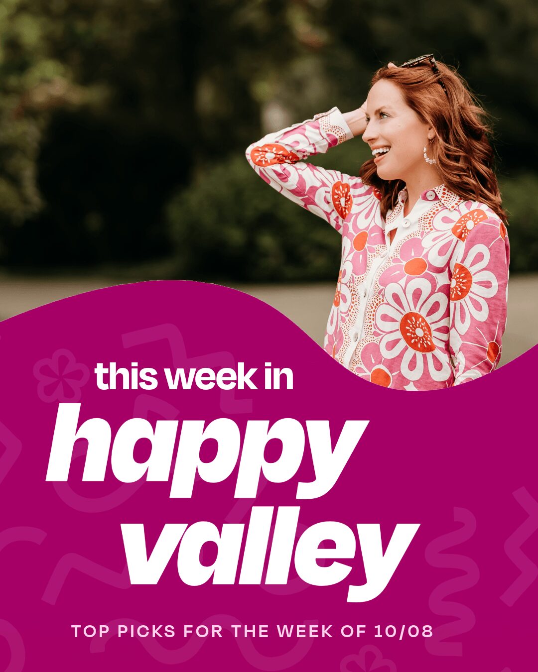 Smiling woman with red hair in a floral dress outdoors, hand on head, cheerful expression.
