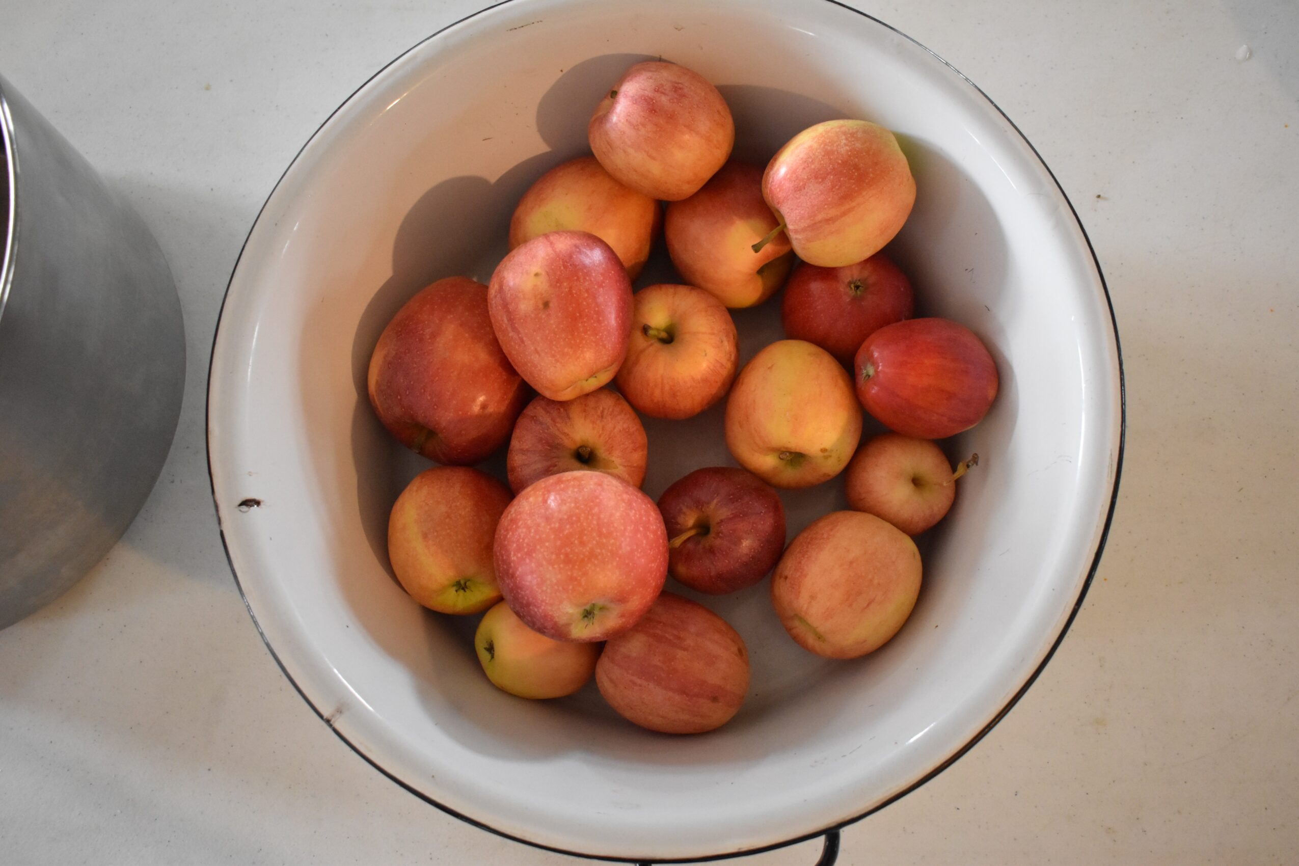 A bowl filled with various red and yellow apples on a light-colored surface.