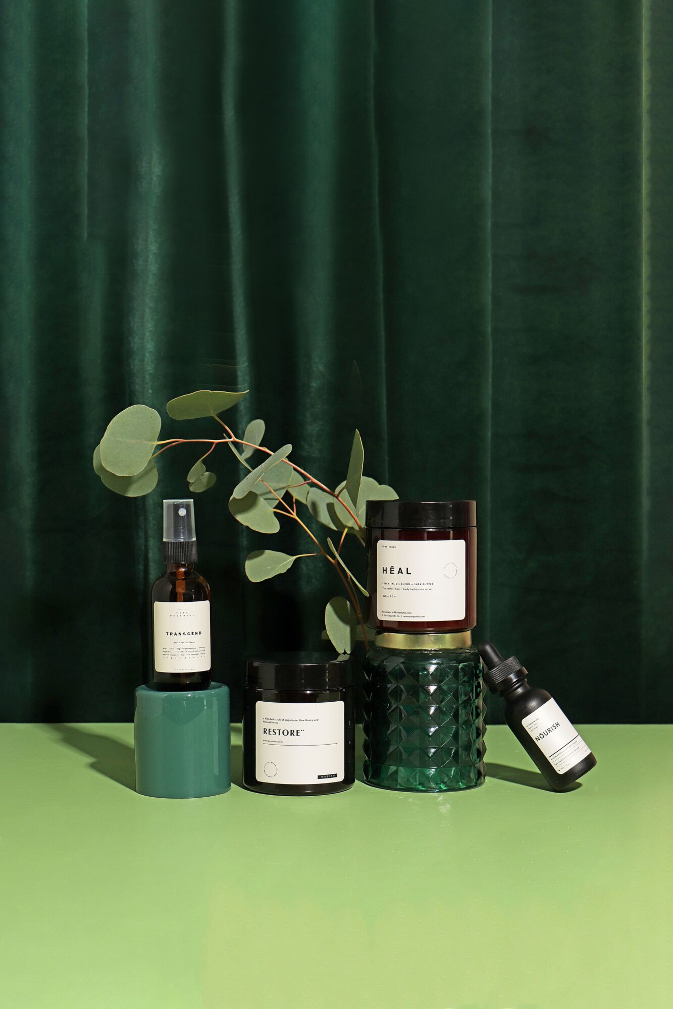 Various skincare and cosmetic products with a plant on a green surface against a dark green curtain background.