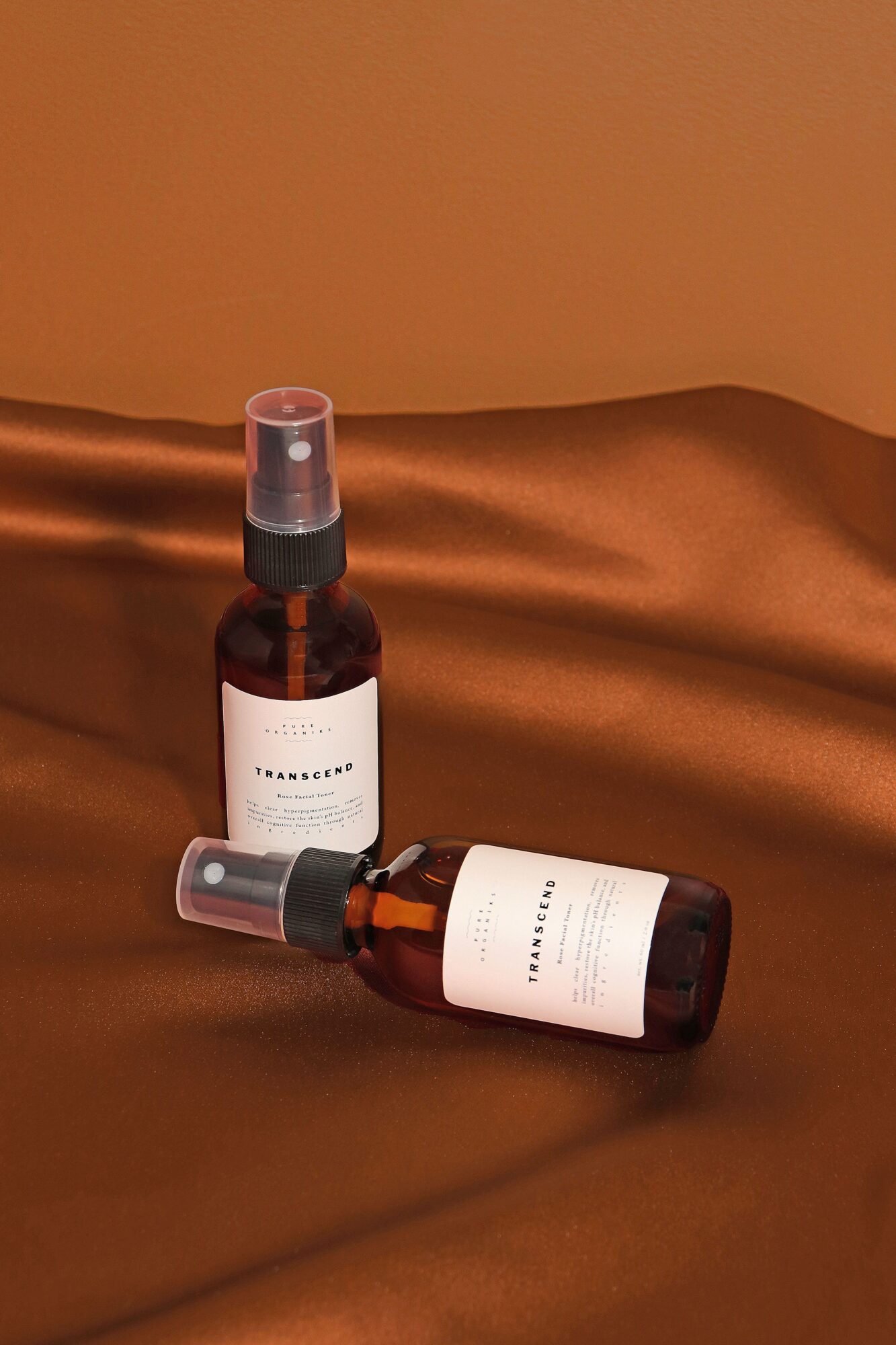 Two brown bottles with white labels and spray caps on a shiny, copper-colored surface.