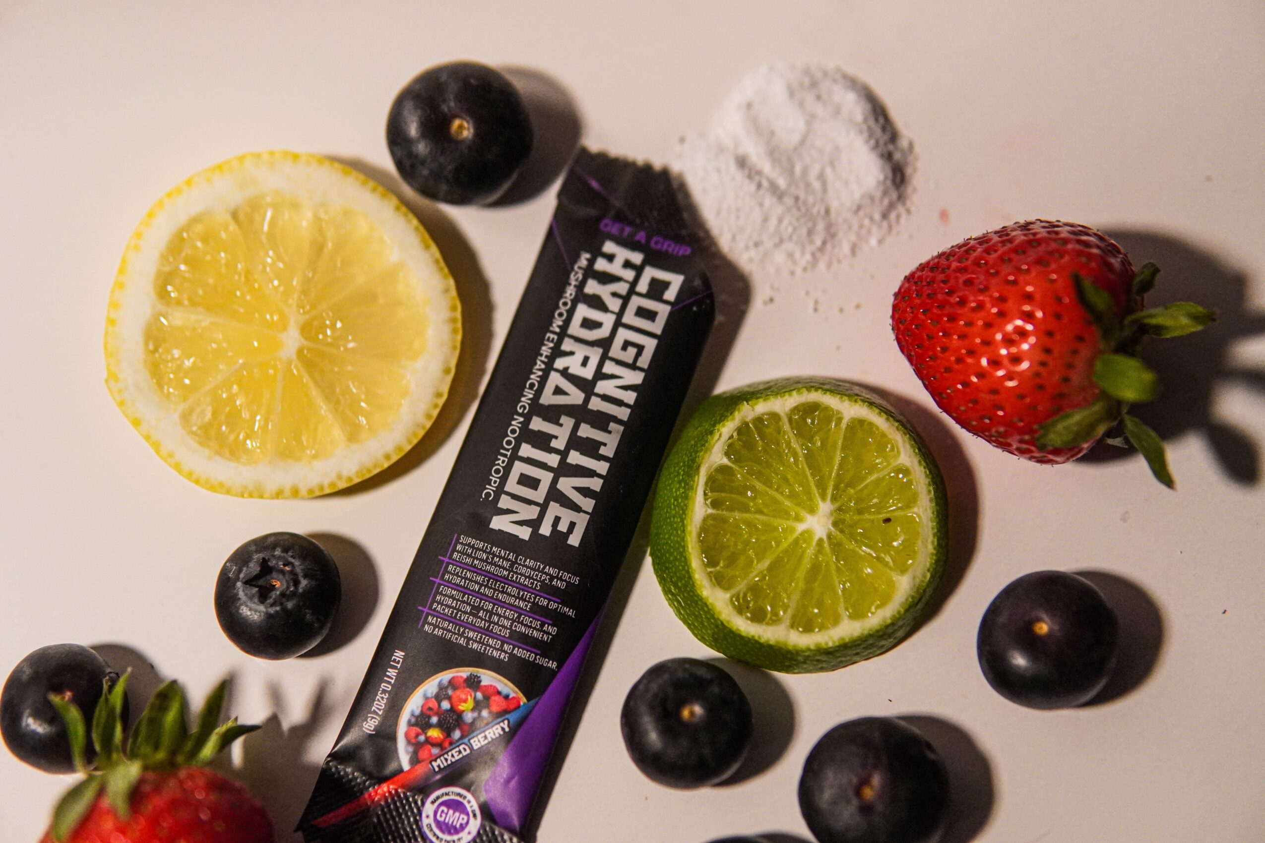 Lemon, lime, strawberries, blueberries, and a black supplement bottle on a white surface.