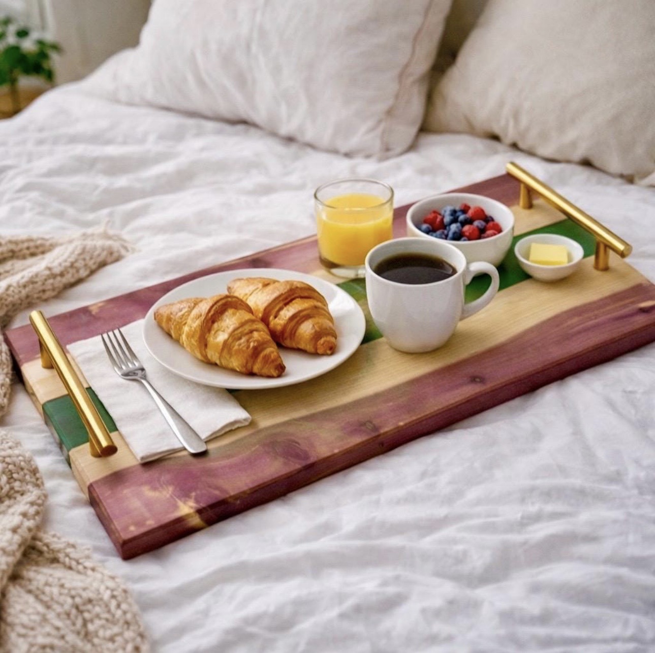 Breakfast tray with croissants, orange juice, berries, coffee, and butter on a bed with white bedding.