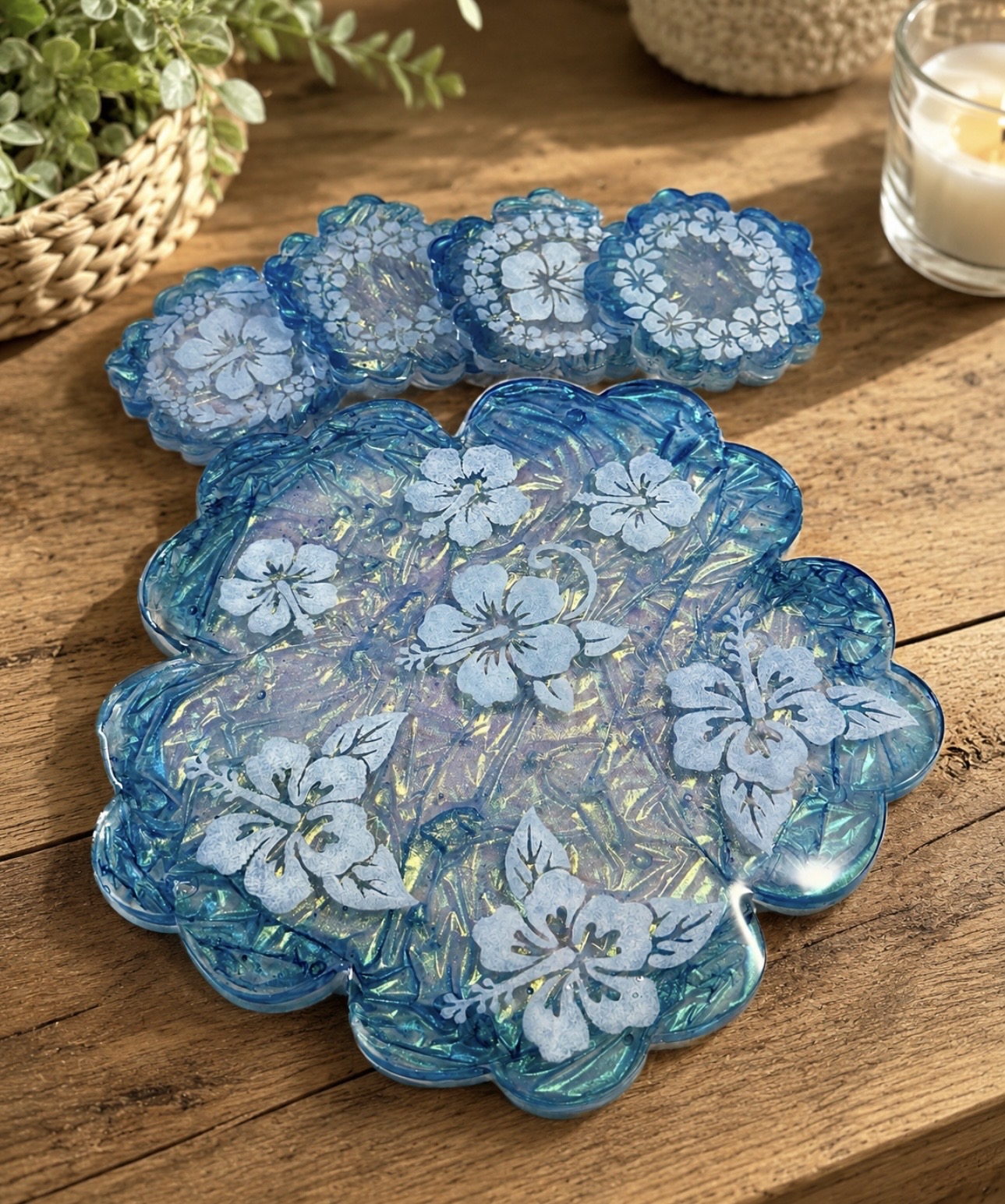 Set of blue glass coasters with floral patterns on a wooden table, with a plant and candle in the background.