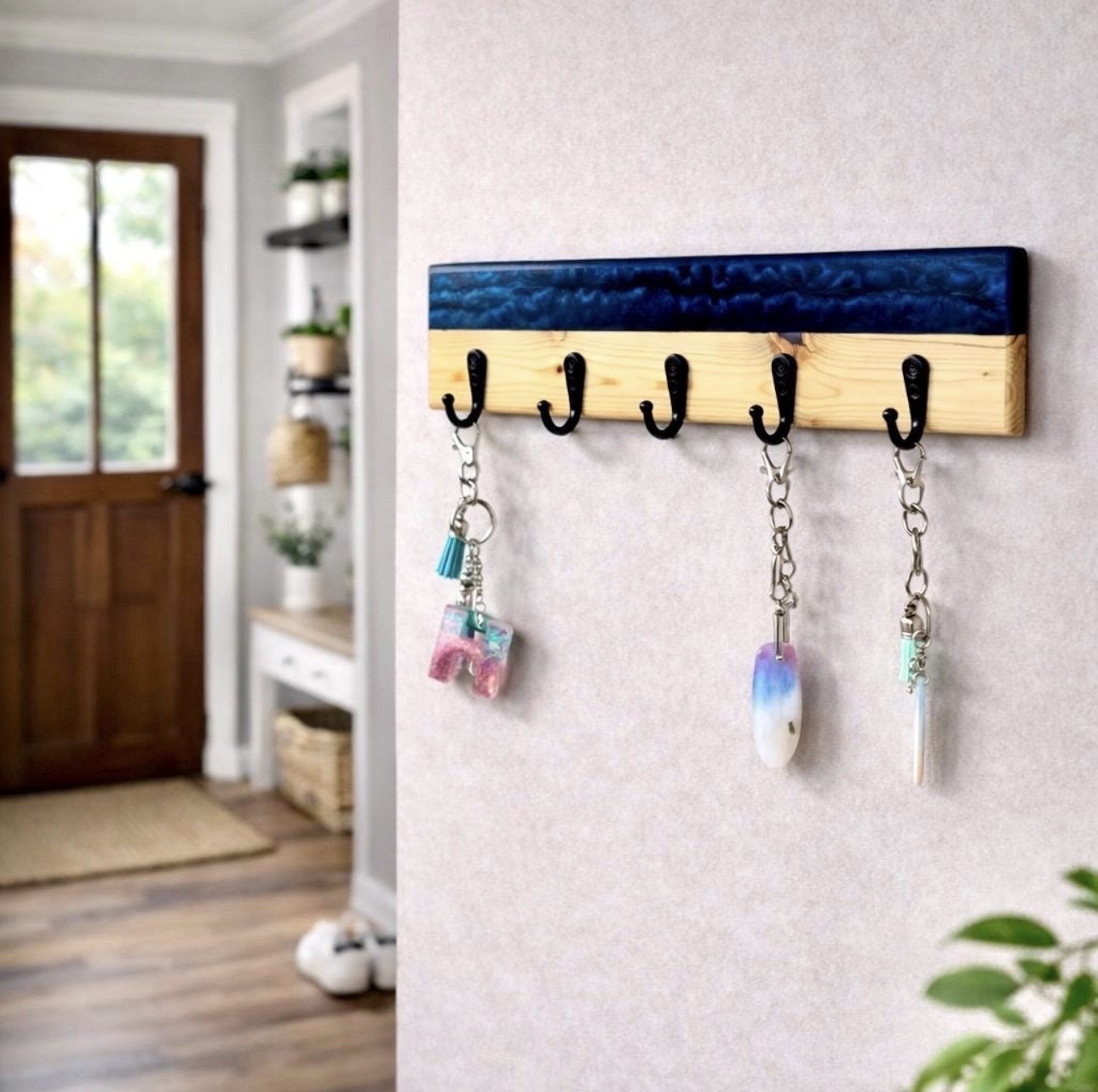Wall-mounted wooden coat rack with five hooks, decorated with blue and natural wood, holding three keychains, in a room with a door and shelves.