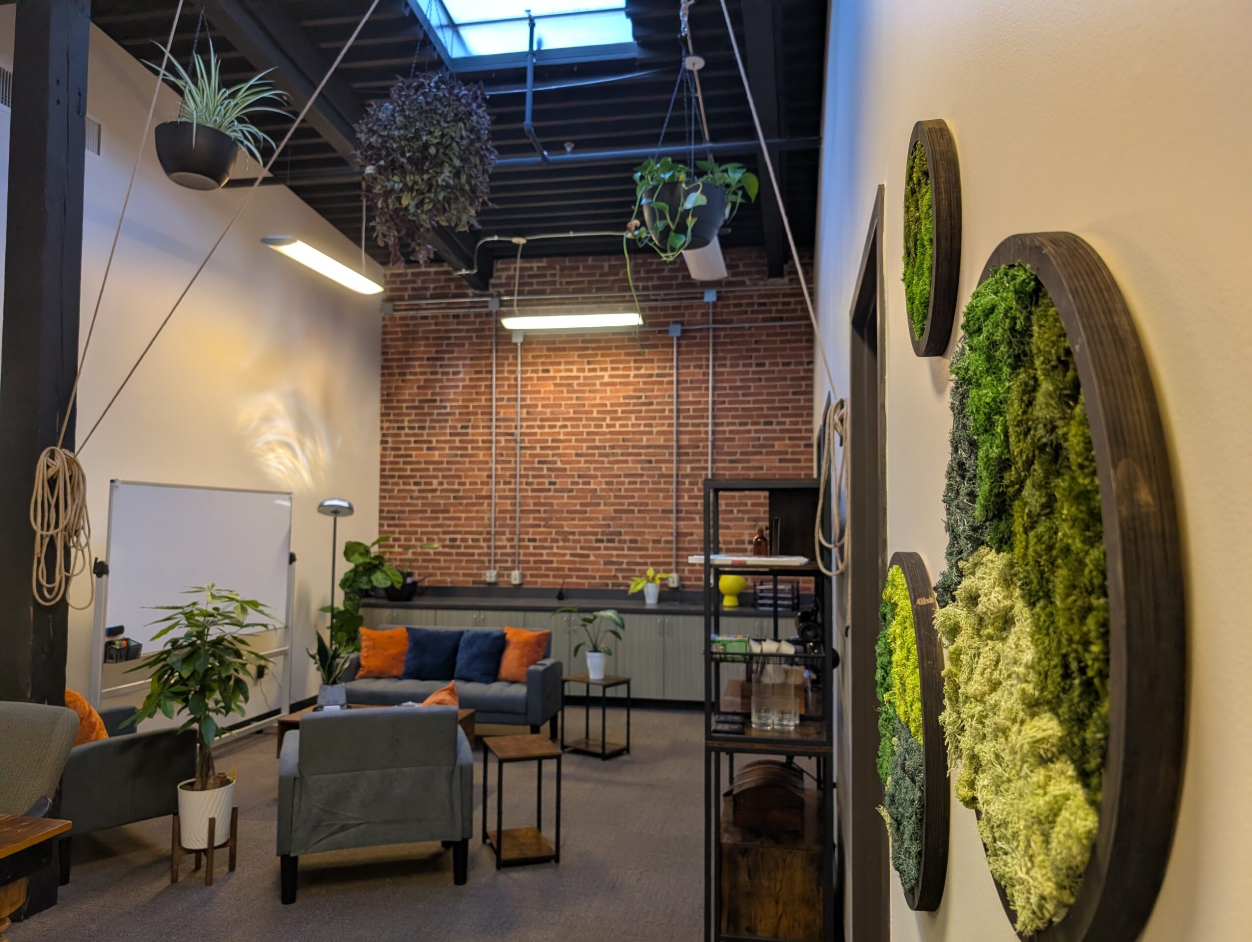 Interior of a modern room with brick wall, hanging plants, seating area, and green moss wall art.
