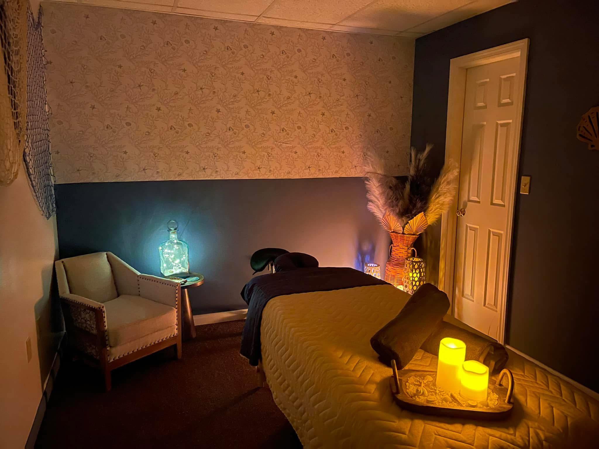 Room with a bed, armchair, door, and decorative lighting, including candles and a vase with flowers, in a cozy setting.