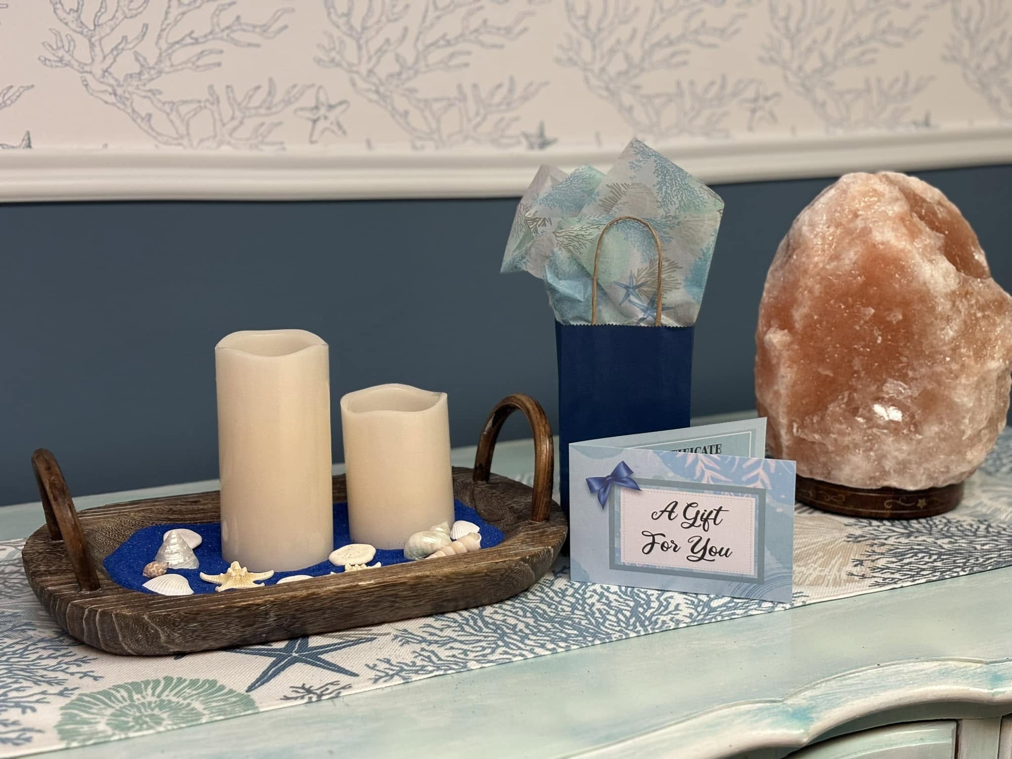 Decorative display with candles, a salt lamp, and a gift card on a table, with a patterned wallpaper background.