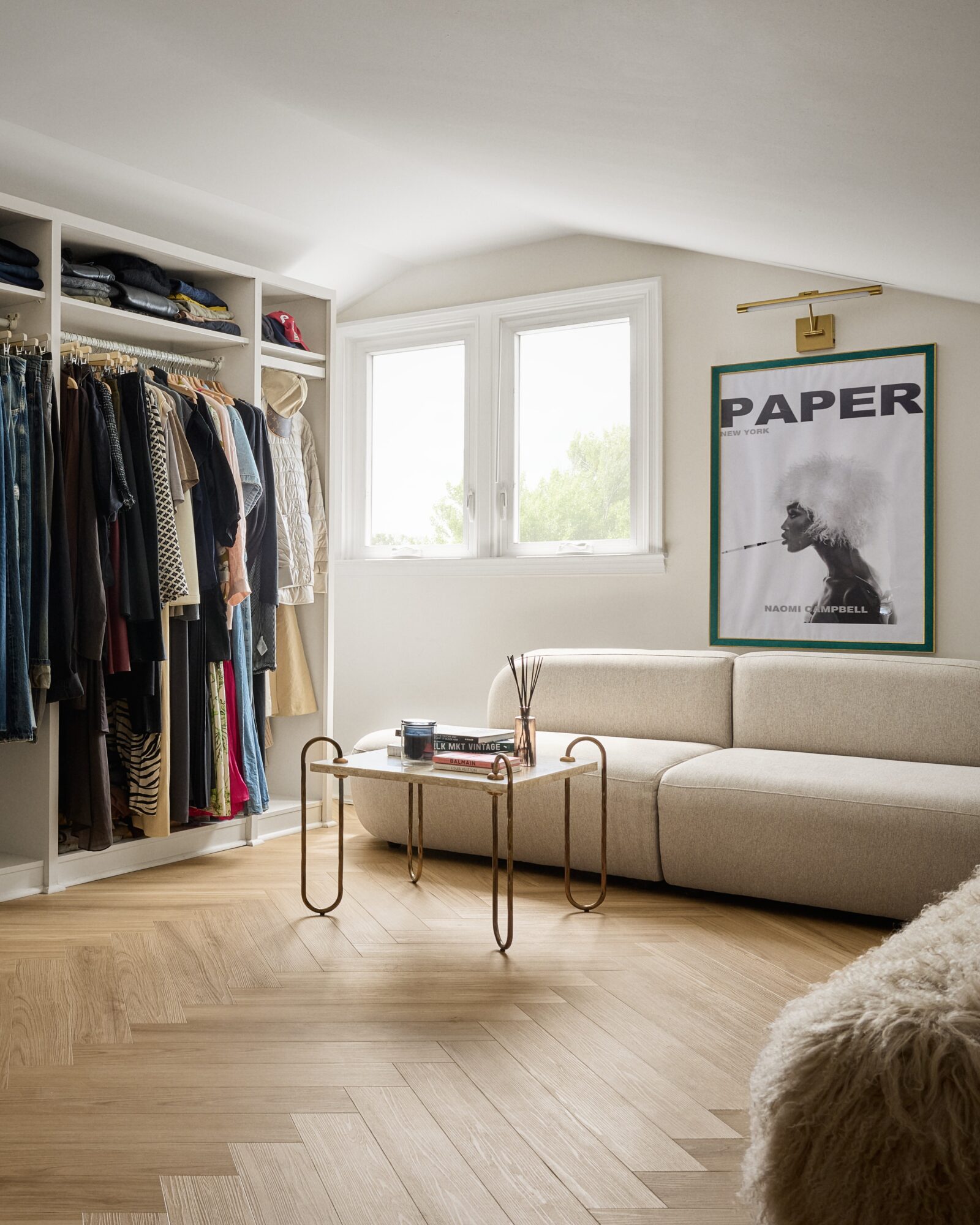 Living room with a large window, beige sofa, open closet with clothes, and framed artwork on the wall.