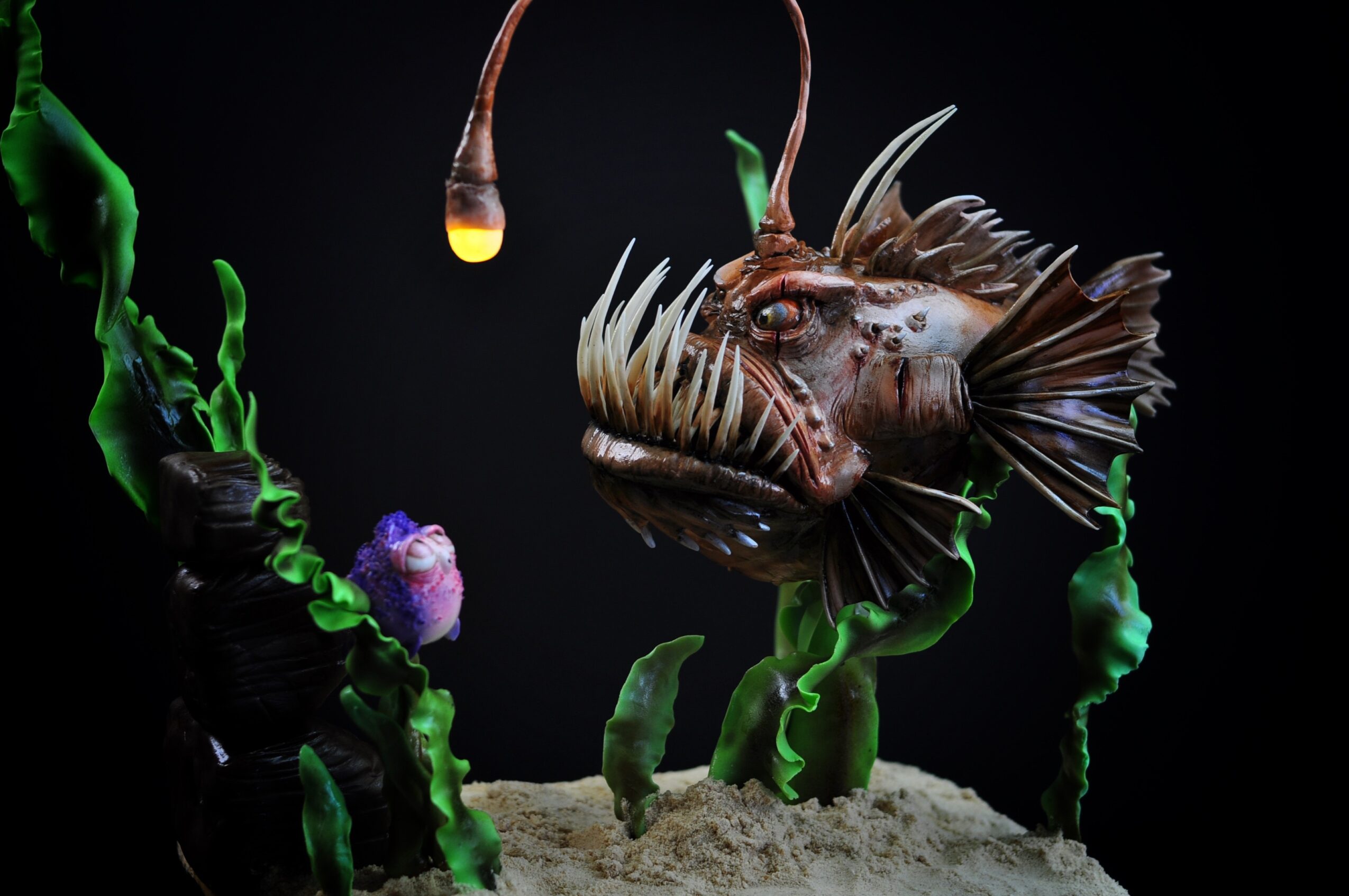 Aquatic creature with spiky fins and long antennae, surrounded by green plants and a purple coral, against a dark background.