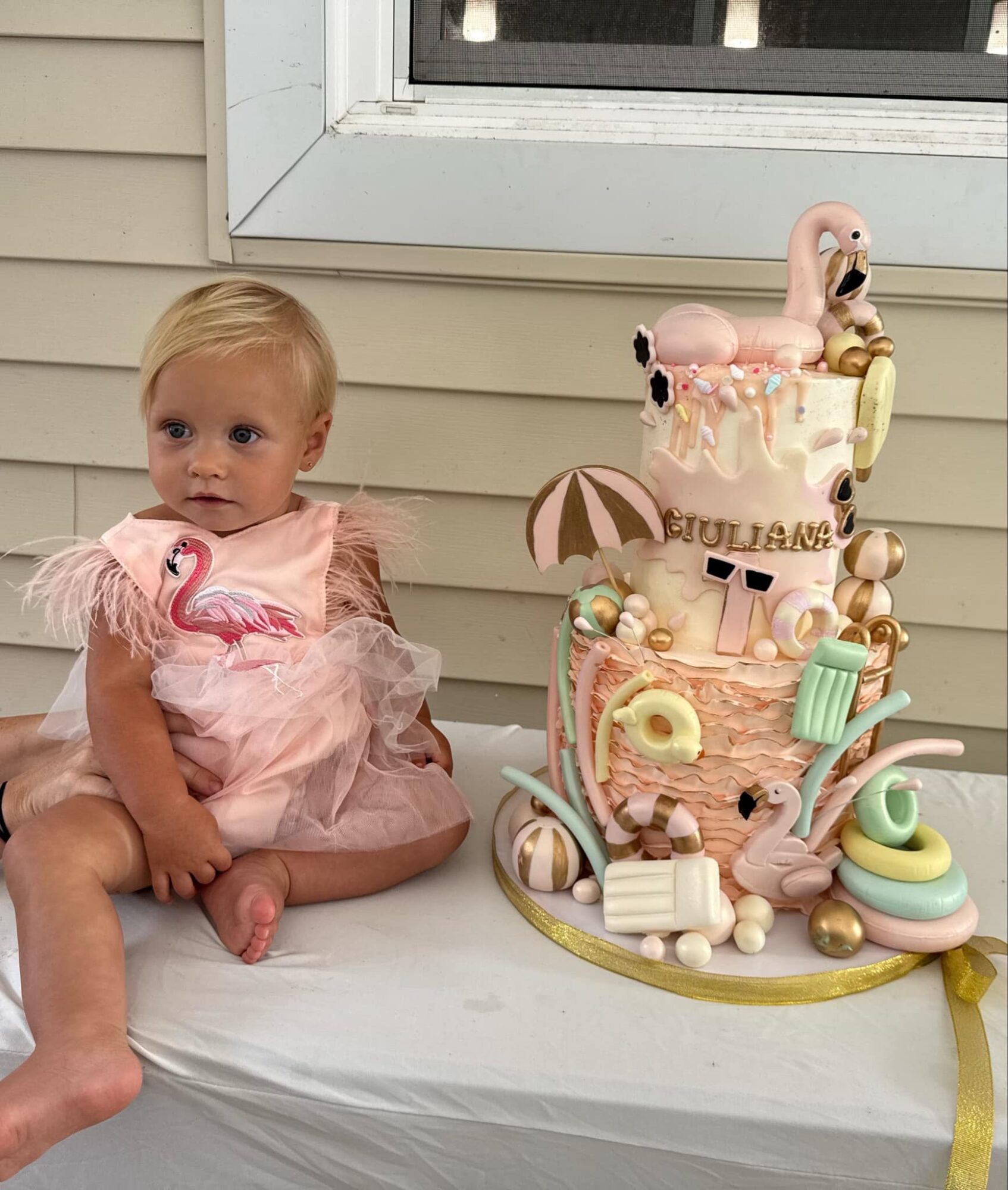 Child in pink dress sitting on a table next to a decorated cake with swan topper and pastel colors.