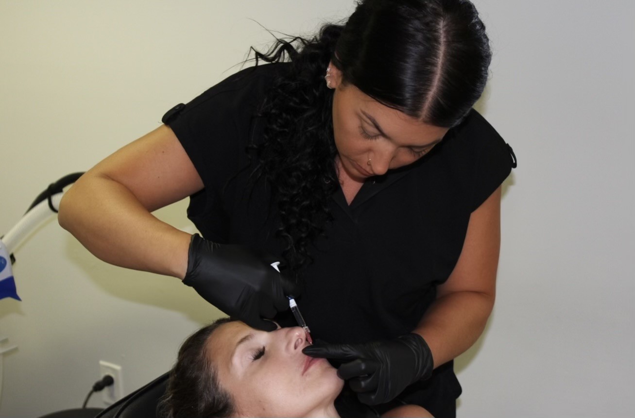 Woman performing a dental procedure on a patient lying down, wearing black gloves and a black top.