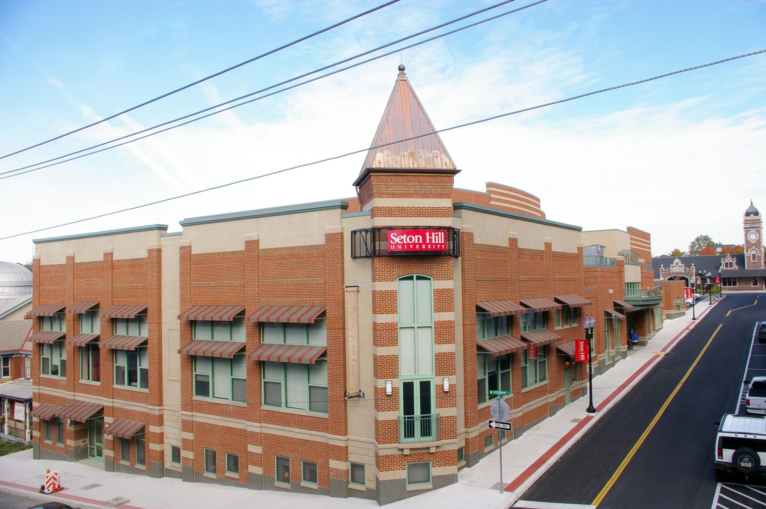 Corner of a brick building with a pointed turret, digital sign, and street view with parked cars and sidewalk.
