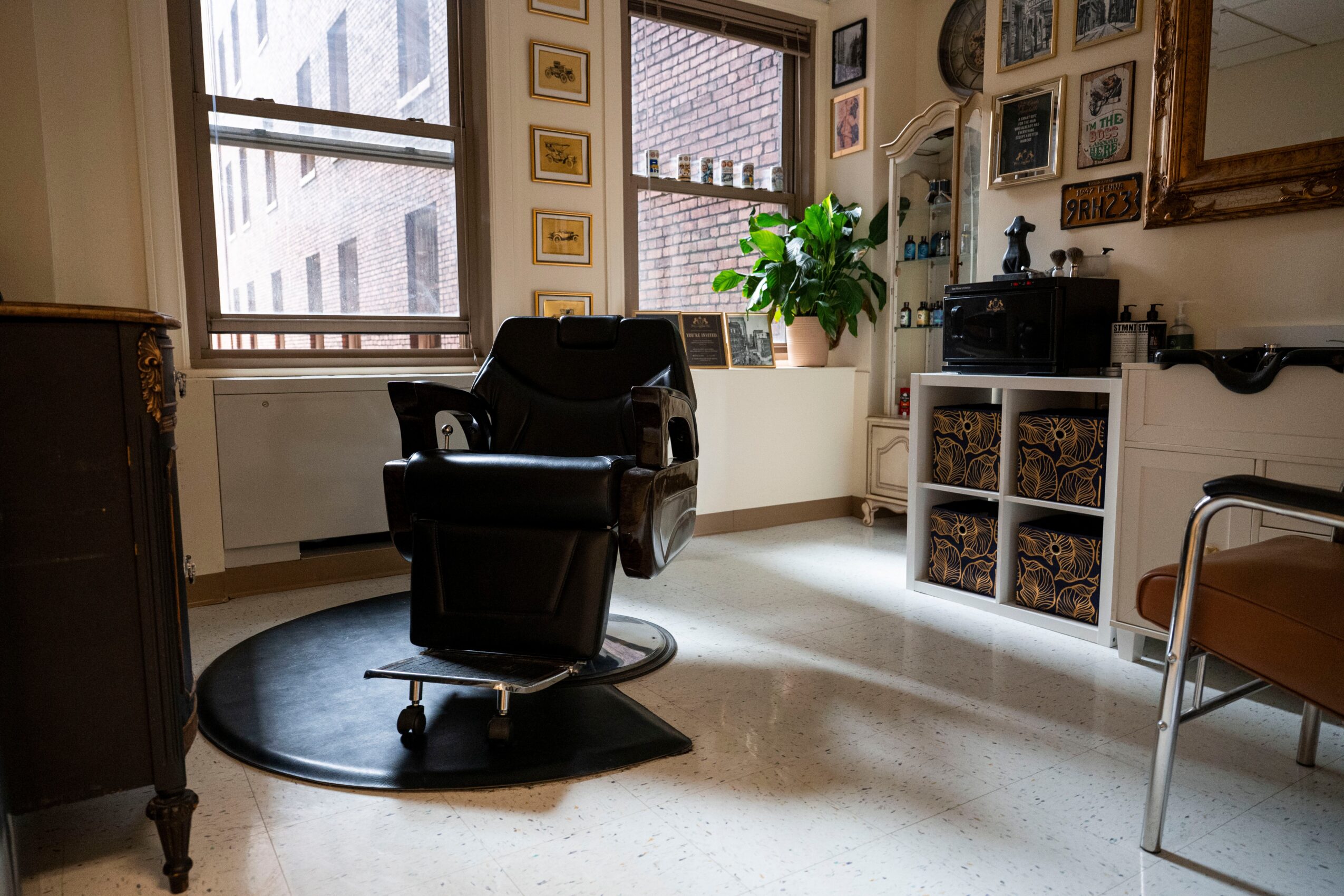 Black office chair on a circular rug in a room with windows, plants, and framed pictures, sunlight streaming in.