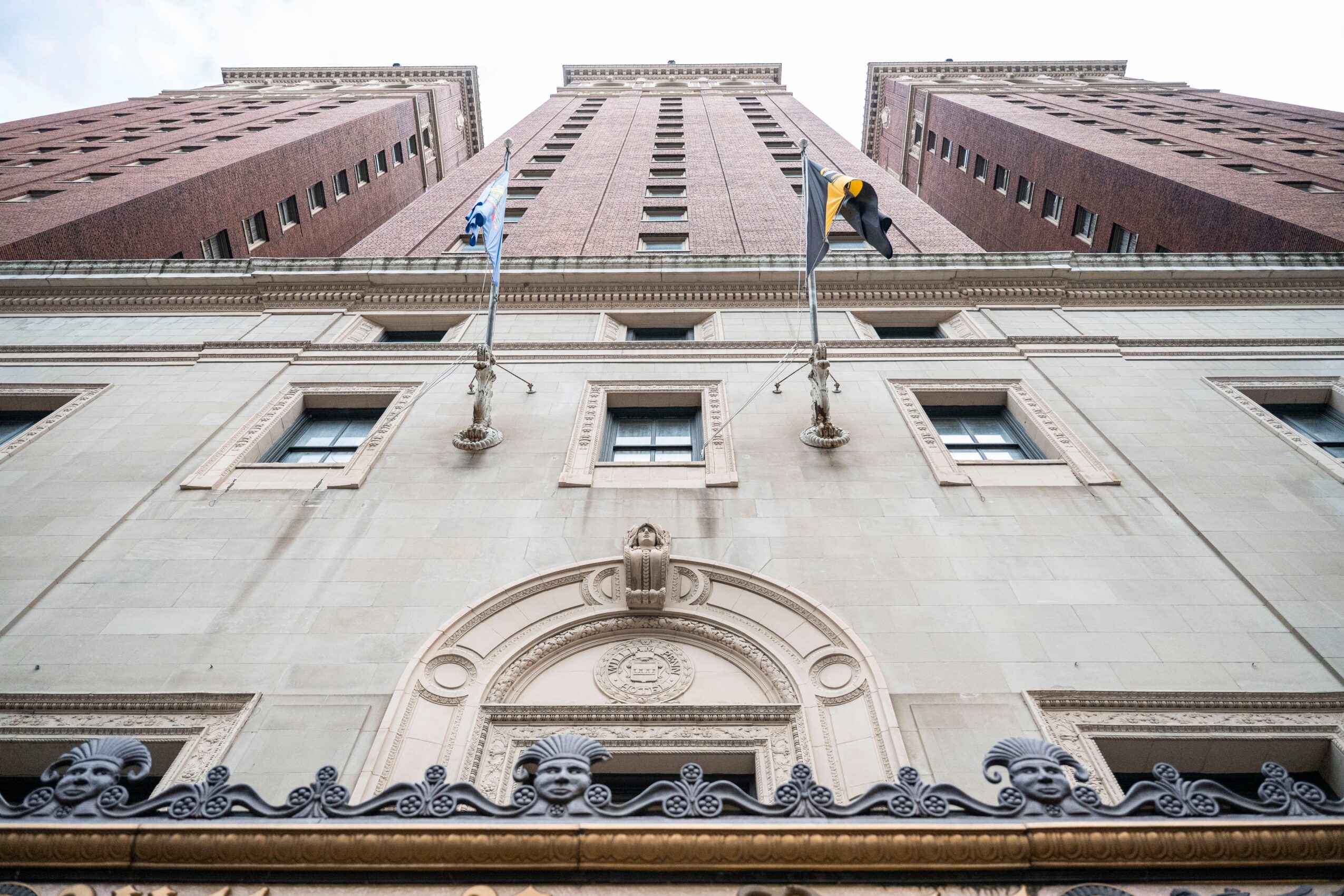 View of a tall building from below, showing the facade with flags and architectural details, against a cloudy sky.