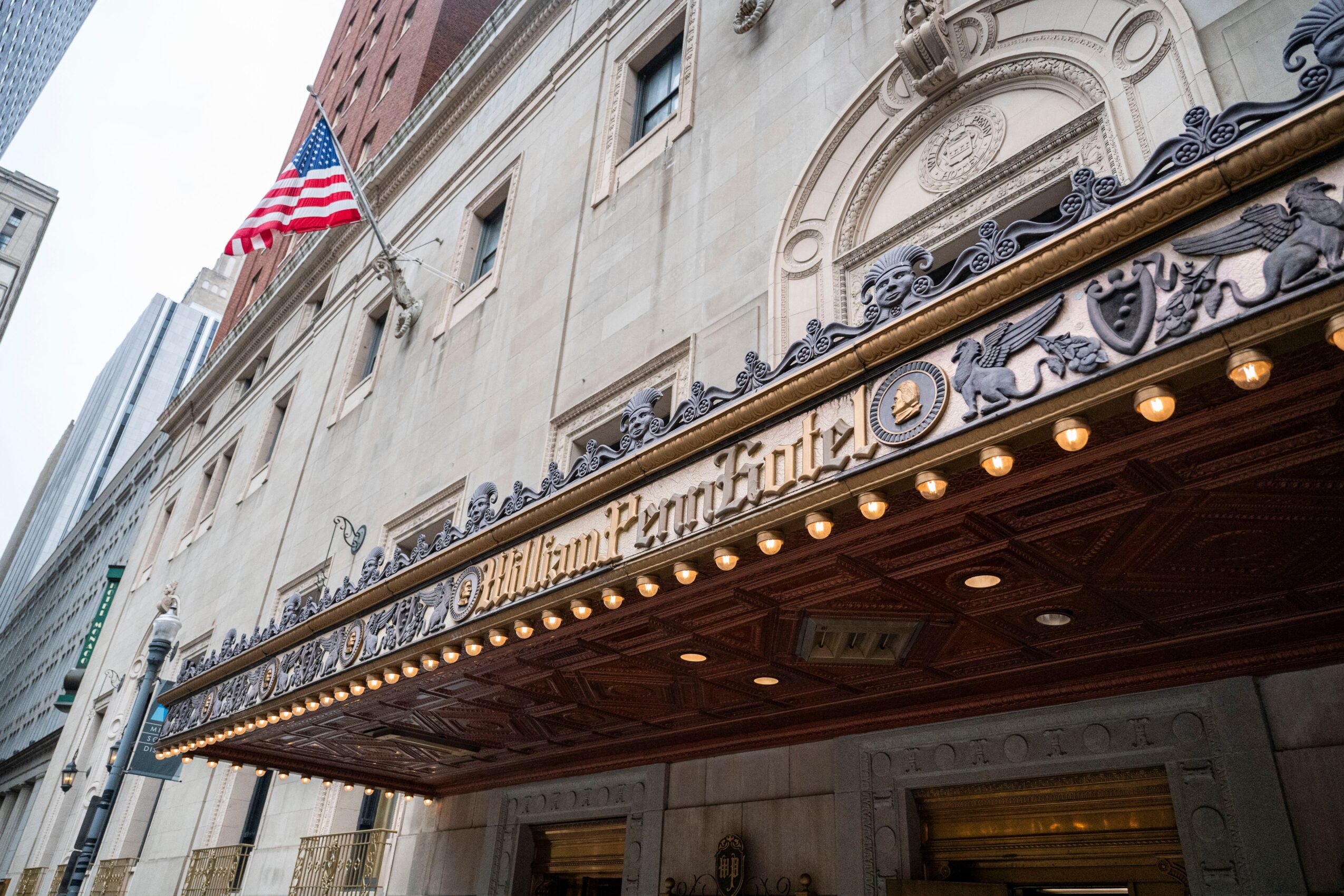 The building's facade features an ornate entrance with a marquee and decorative elements, with an American flag above. Wording is partially visible.
