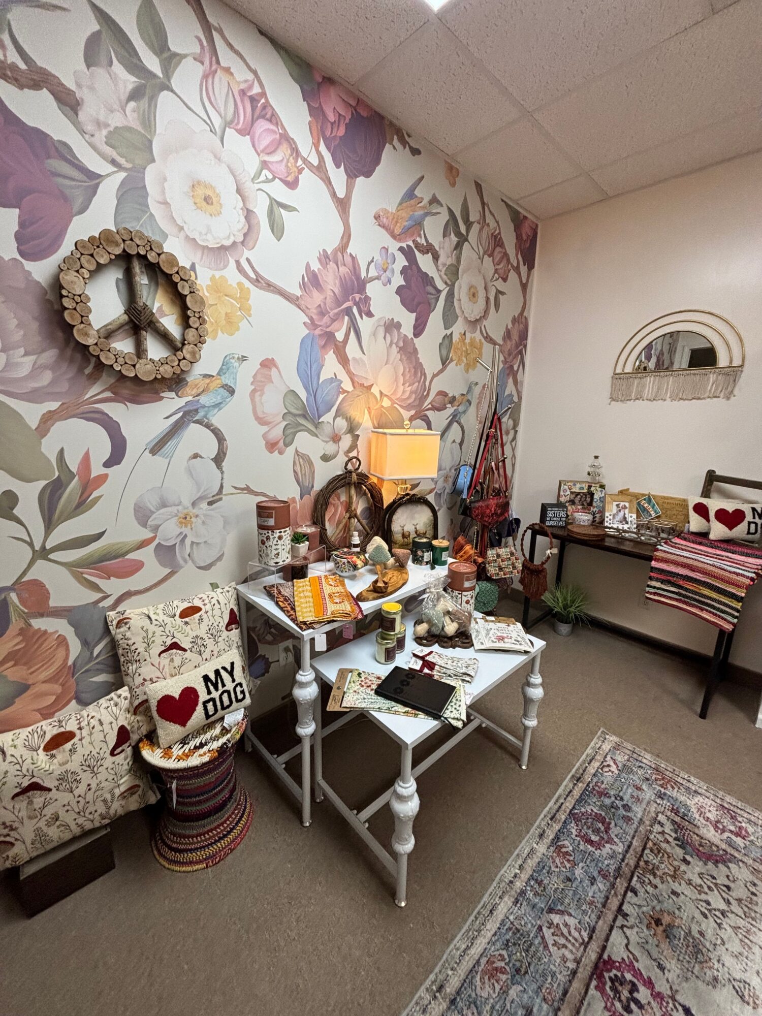Living room with floral wallpaper, a small table with various items, a mirror, and a rug.