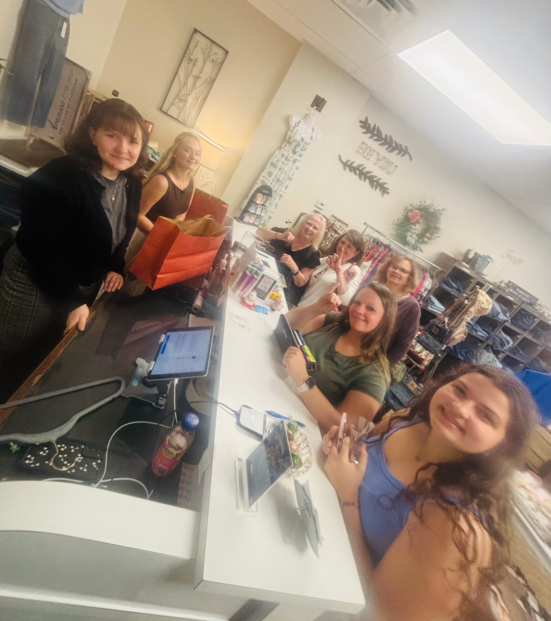 Group of women sitting around a table in a room with shelves and decorations, smiling at the camera.