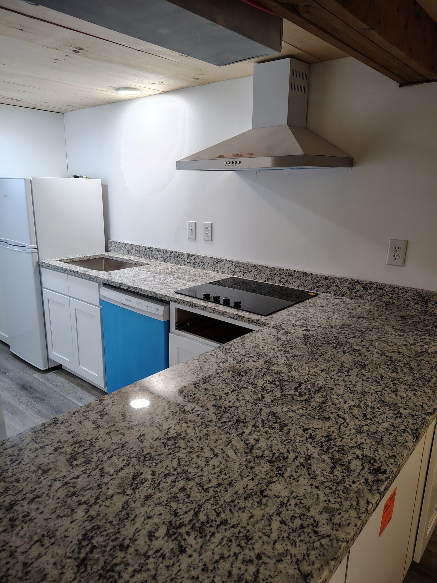 Kitchen with granite countertop, white cabinets, and a stove with a range hood, viewed from the side.