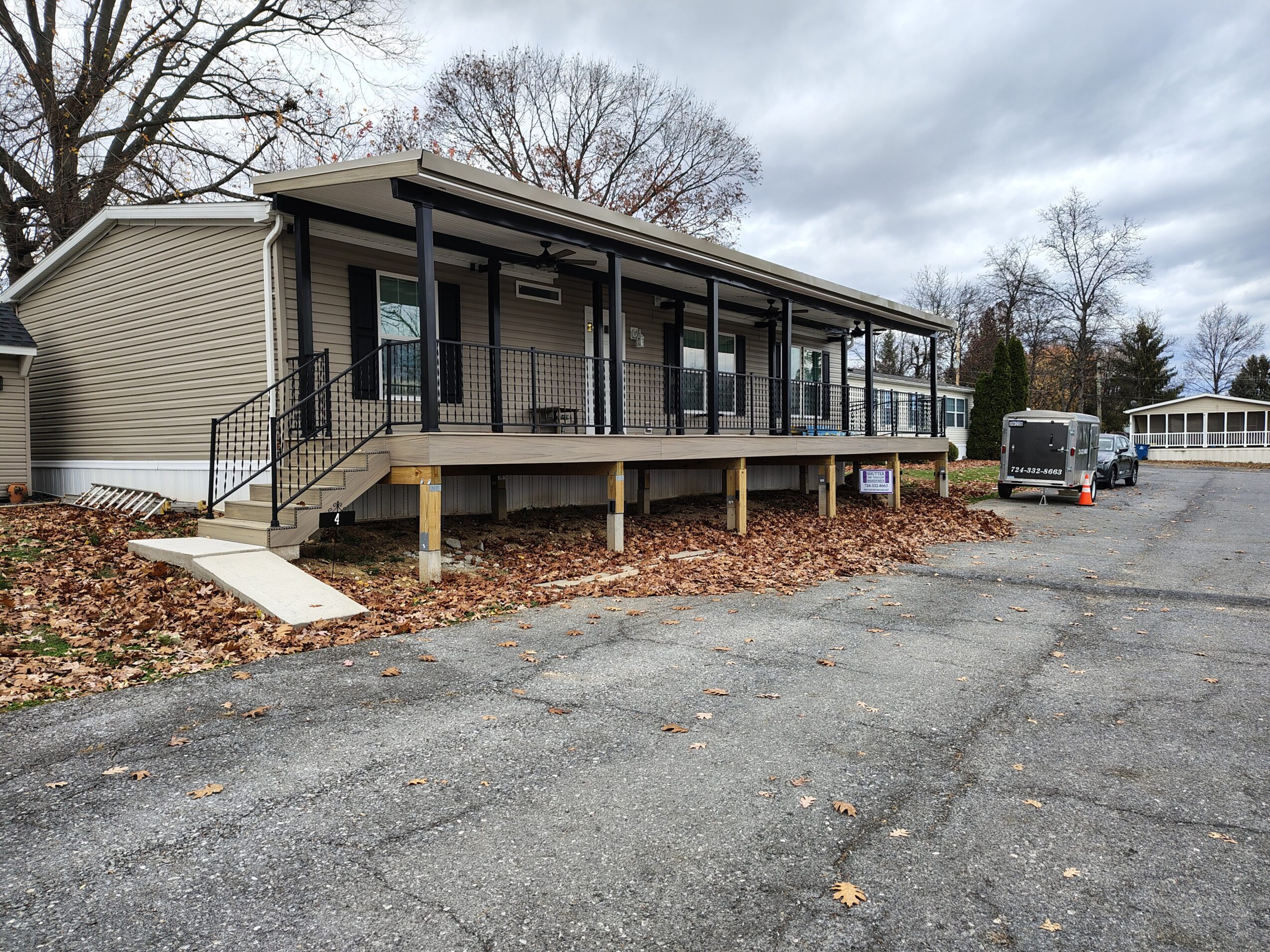 Single-story building with a large covered porch, black railing, and steps leading up to the entrance, surrounded by trees and parking lot.