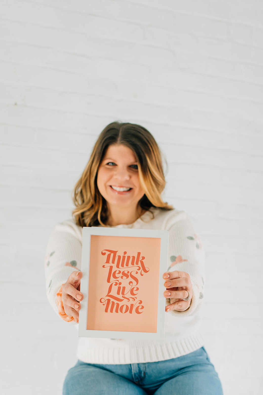 Woman smiling holding a framed sign with orange text, standing against a white wall.