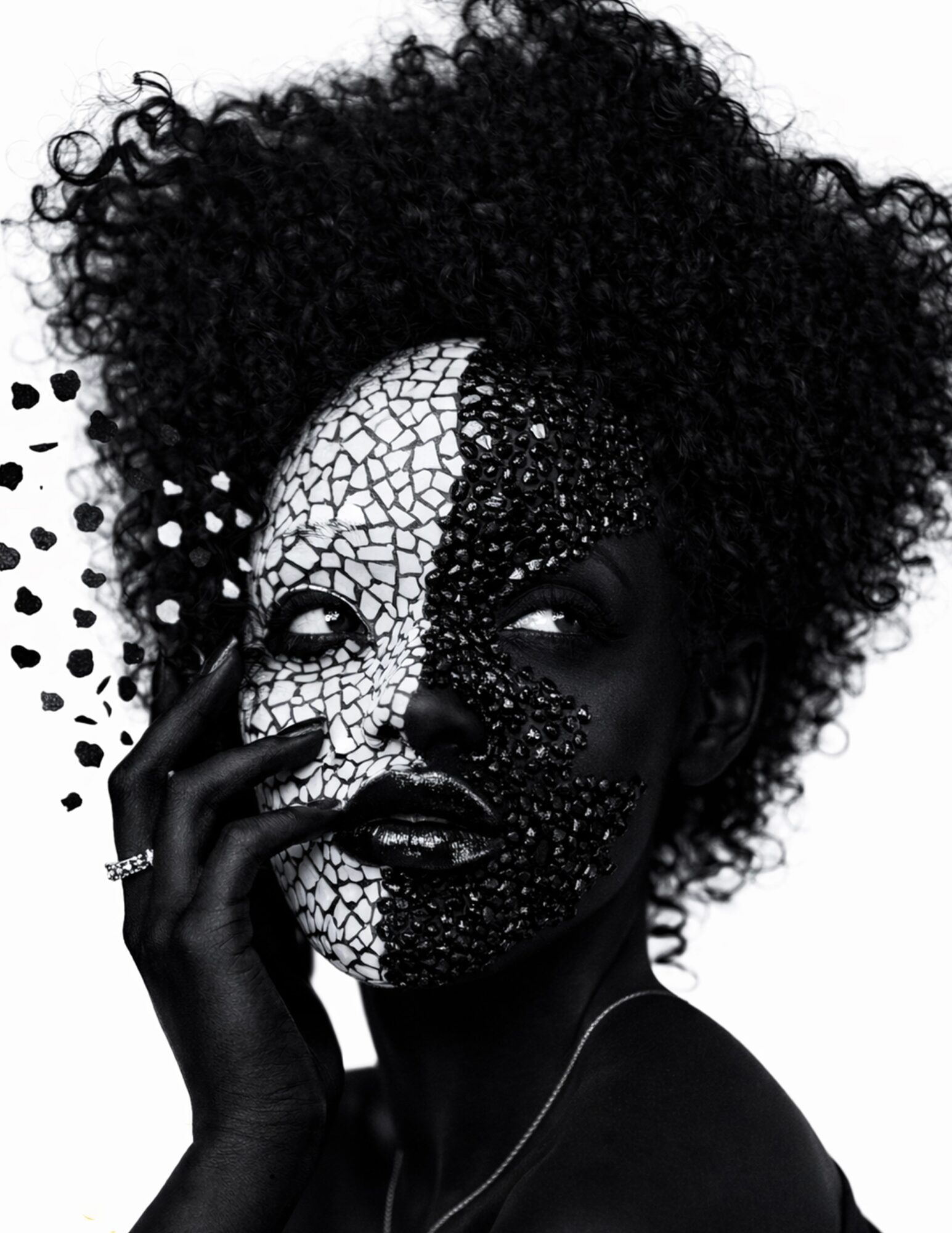 Woman with curly hair and half face painted with cracked pattern, holding her face with her hand, black and white image.