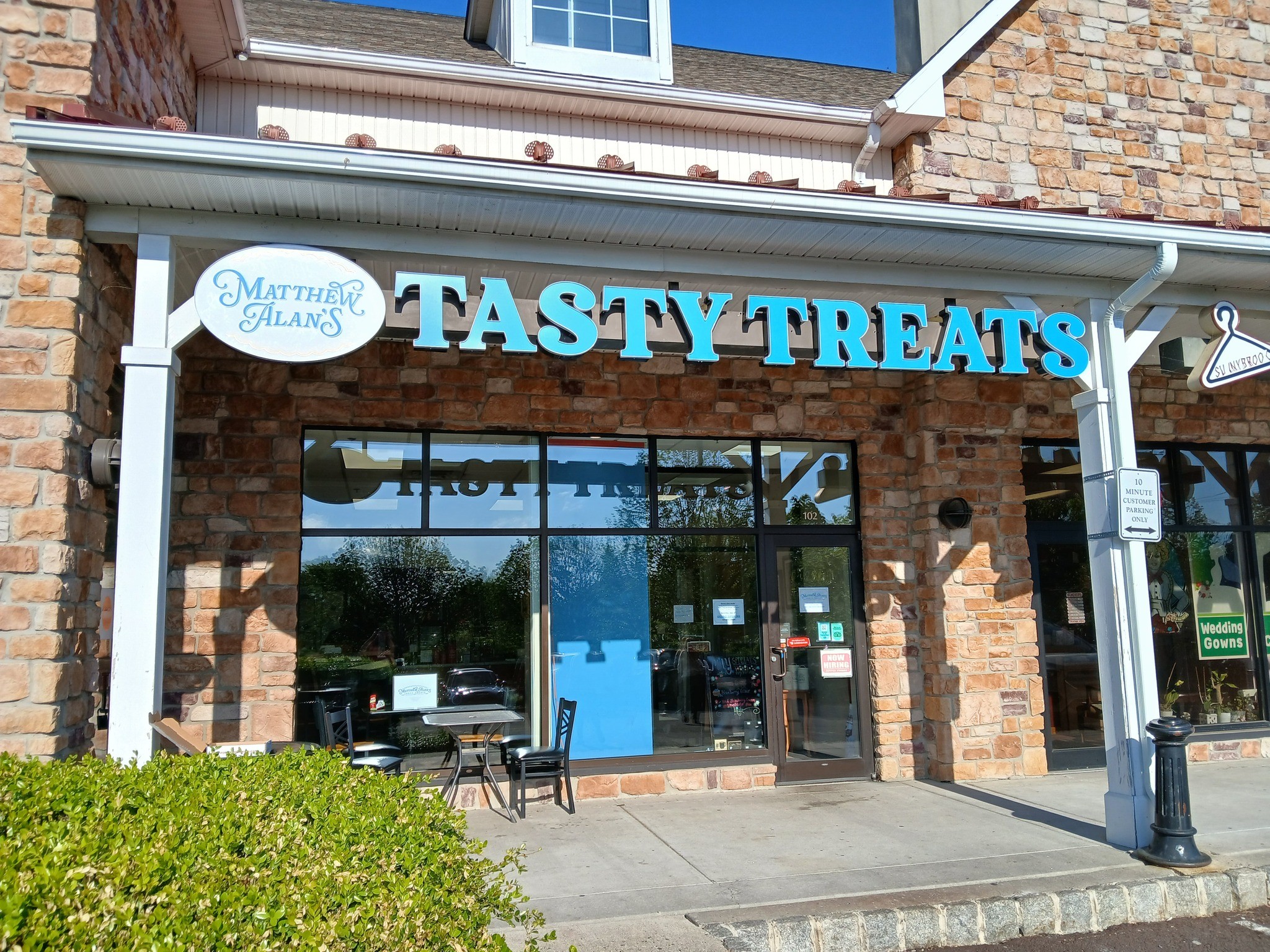 Storefront with a sign reading 'Tasty Treats' and a smaller sign for 'Marina's Cakes' above the entrance, brick exterior, glass door, and windows.