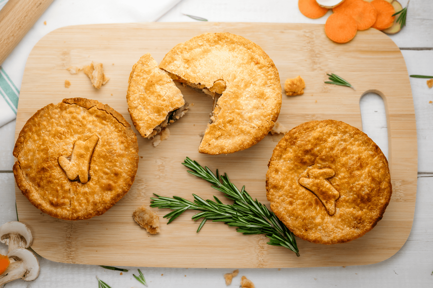 Three fried patties with a sprig of rosemary on a wooden cutting board, one with a bite taken out, and a small piece of carrot in the background.