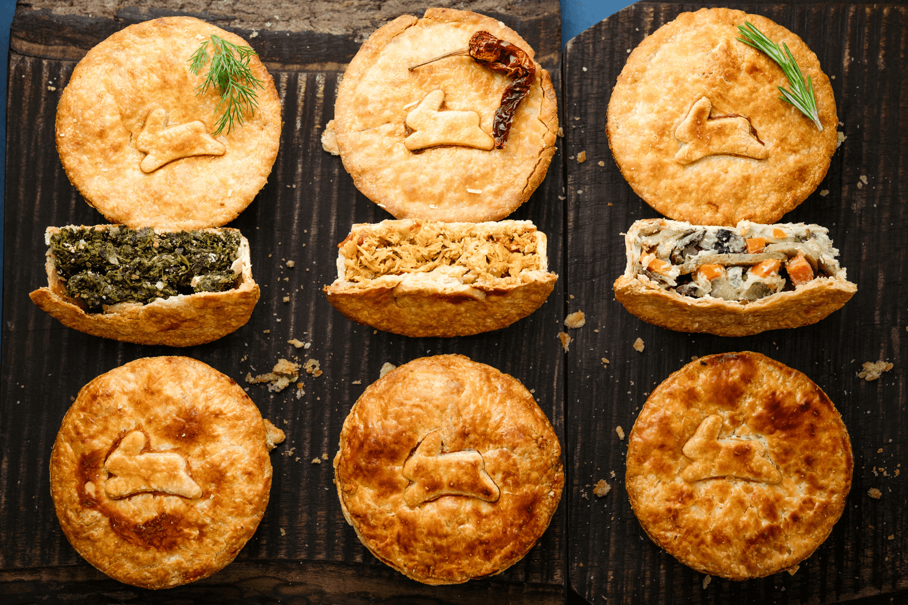 Six fried pastries arranged in two rows, some with fillings visible, garnished with herbs, on a dark surface.