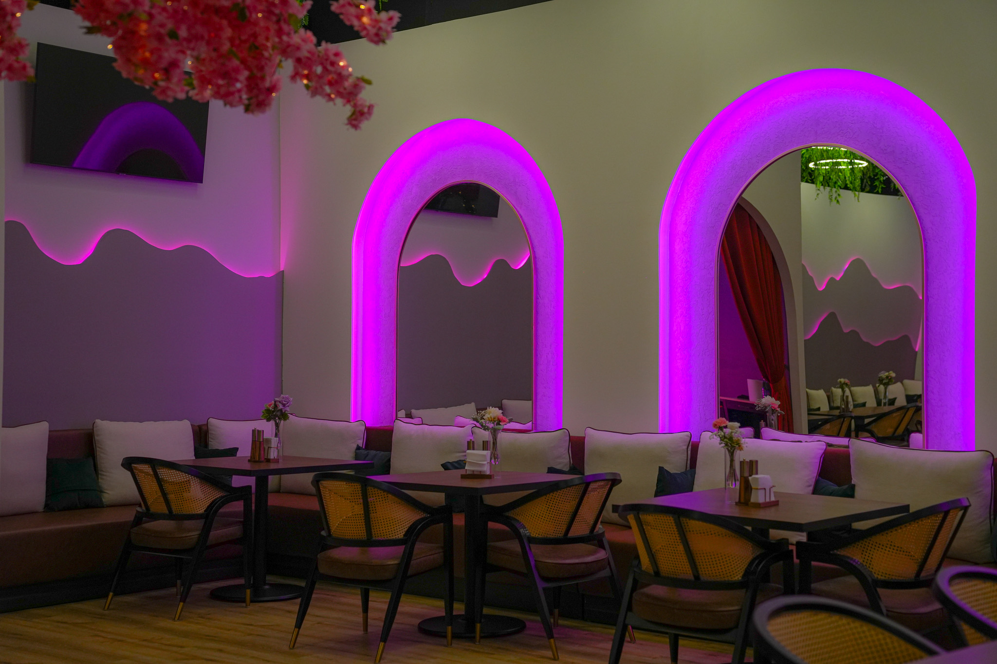 Interior of a restaurant with purple neon-lit arches, tables, chairs, and floral decorations, creating a vibrant atmosphere.