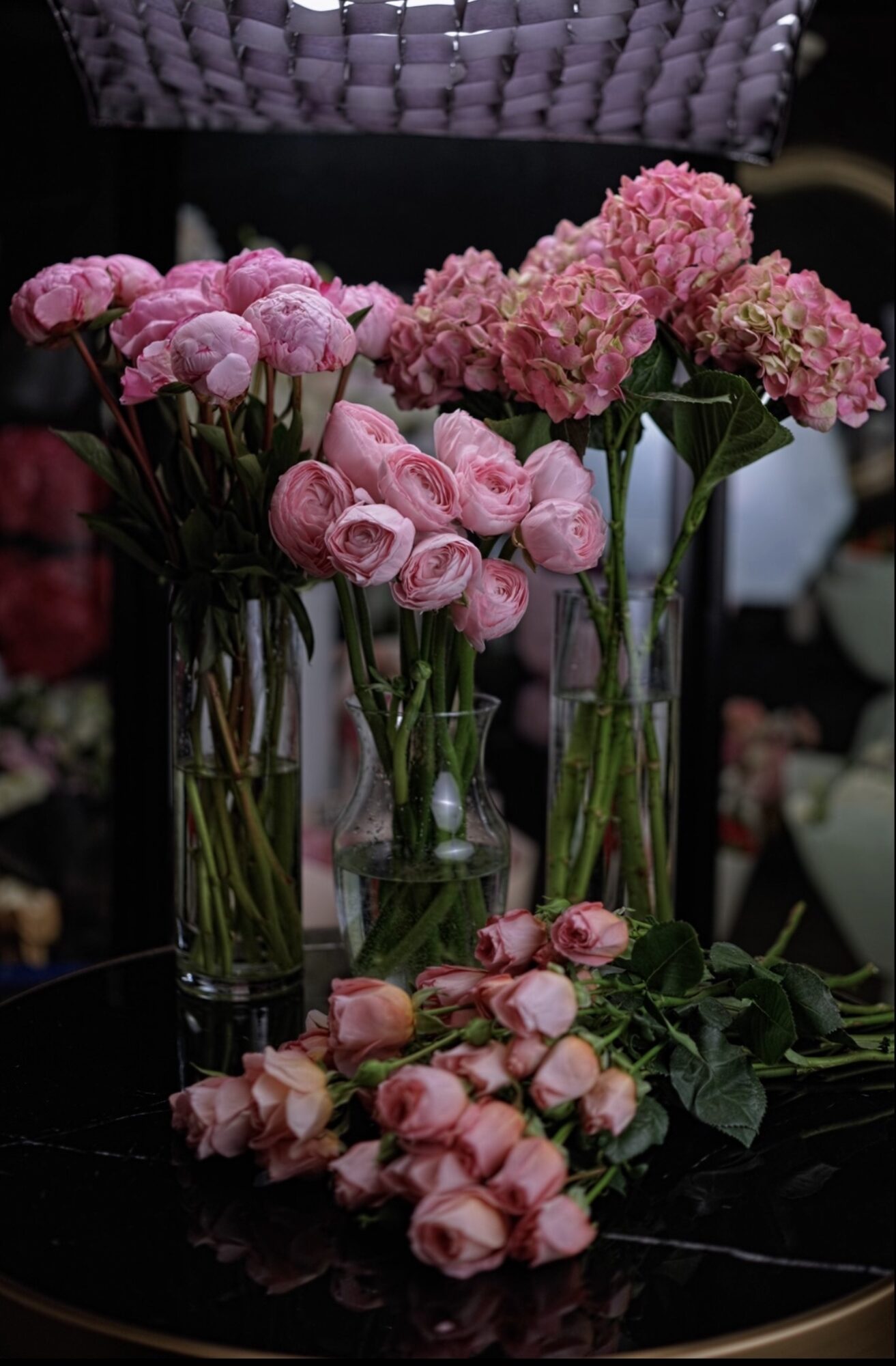 Various pink and purple flowers in glass vases on a dark surface, with some flowers lying down.