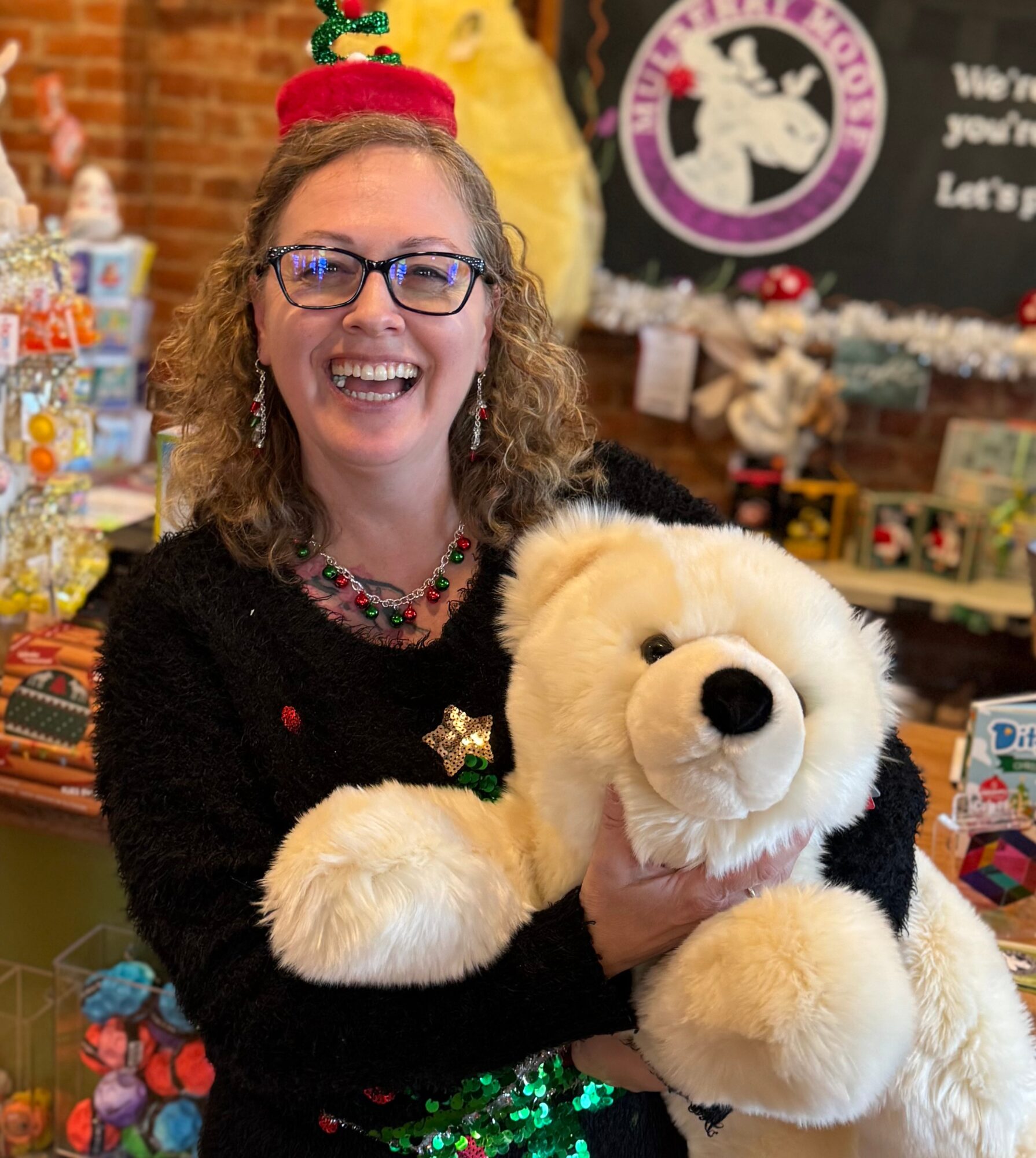Woman smiling, holding a large plush dog, surrounded by holiday decorations and gifts, in a festive setting.
