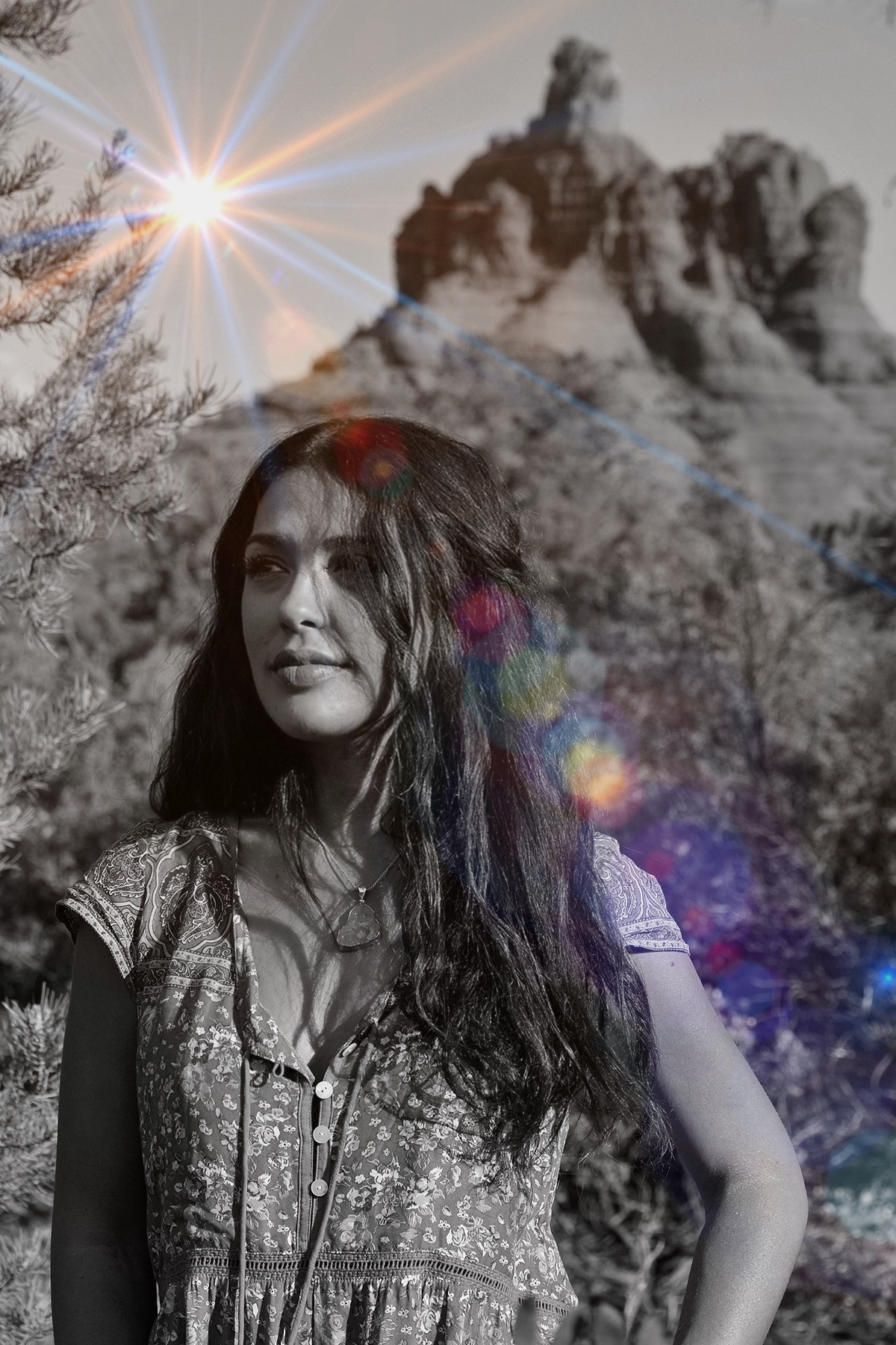 Young woman with long hair outdoors, trees and rocky formations in background, sunlight shining brightly, colorful lens flare effects.