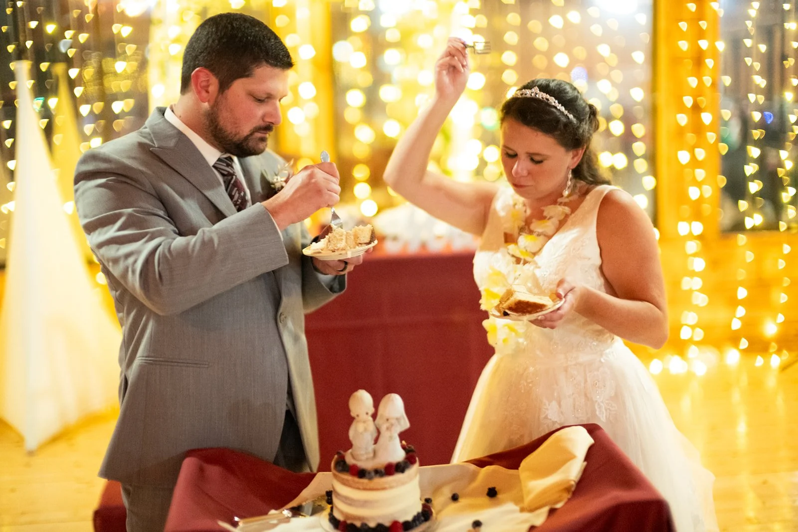 A man and woman at a celebration, with a decorated cake and festive lights in the background.