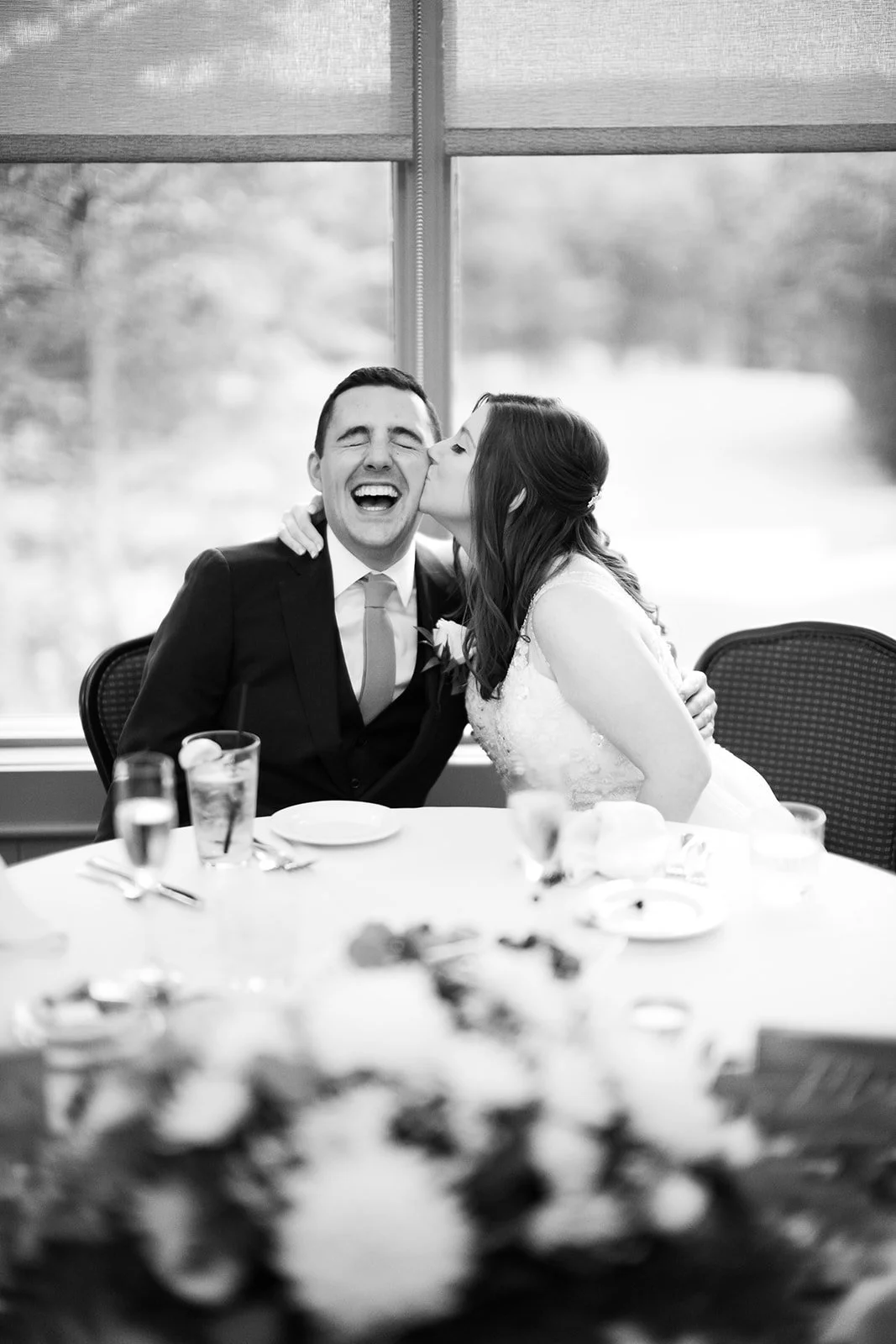 Two people, one in a suit and the other in a dress, share a joyful moment at a table with food and drinks.
