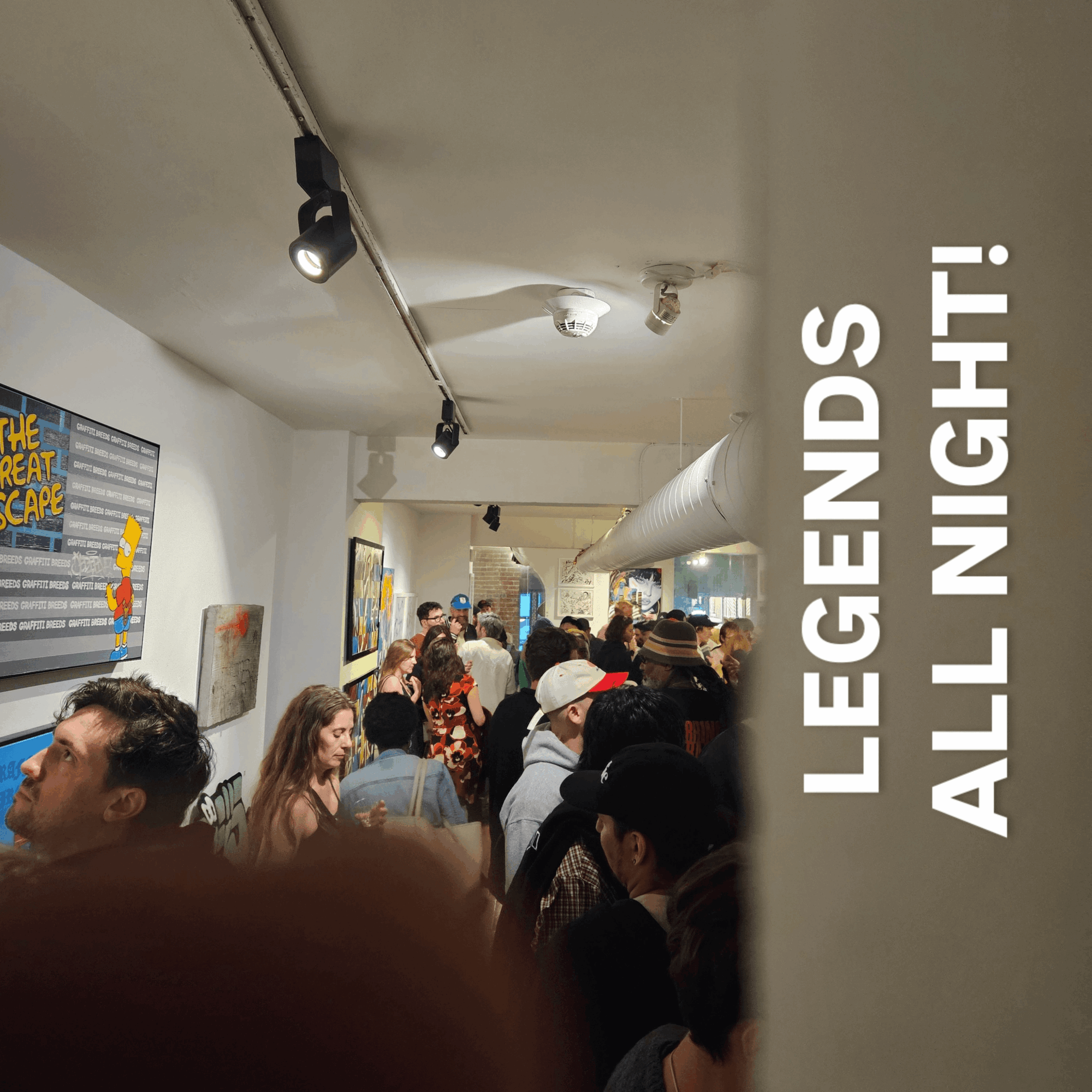 Crowd of people inside an art gallery or event space, with artwork on the walls and overhead lighting, viewed from the side.