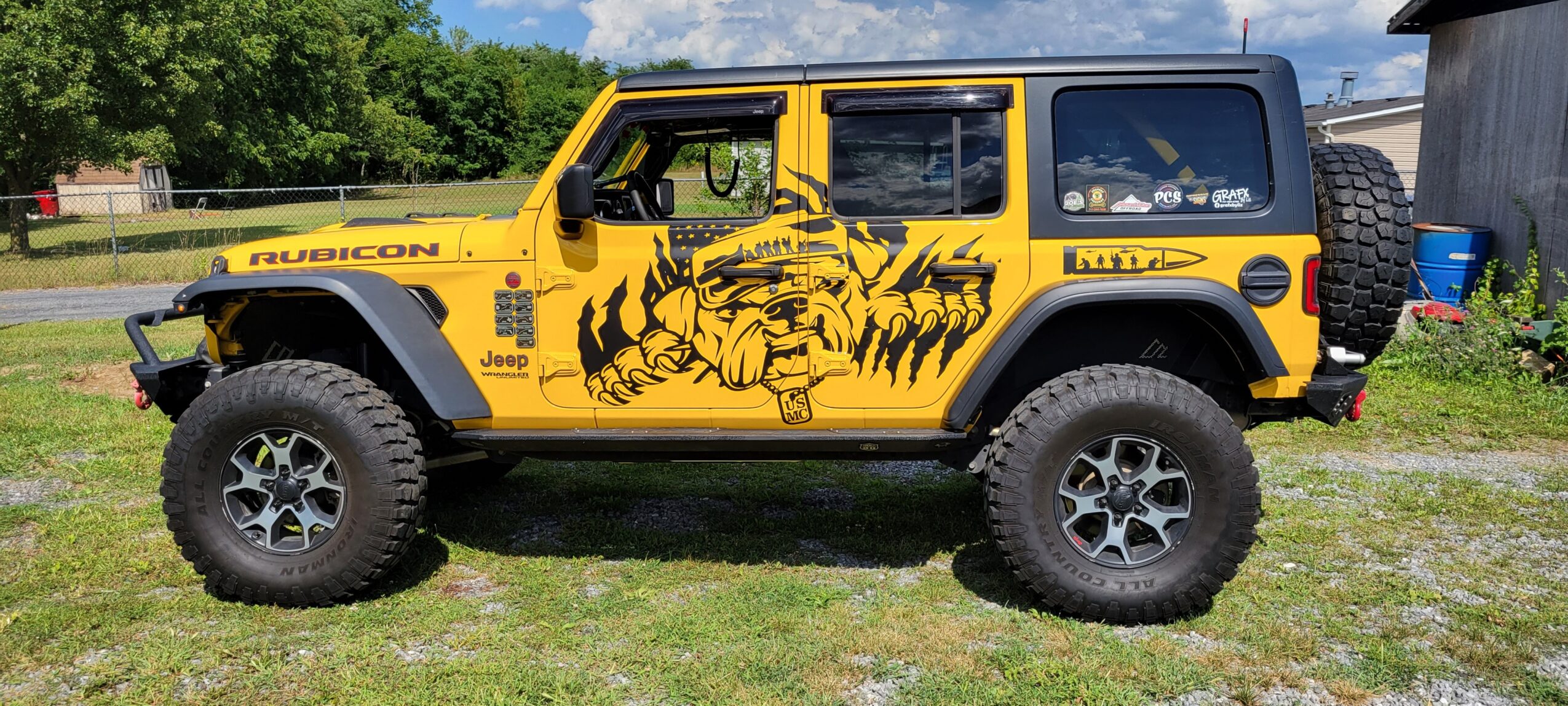 Yellow off-road vehicle with a black tiger graphic on the side, parked on grass with trees and a building in background.
