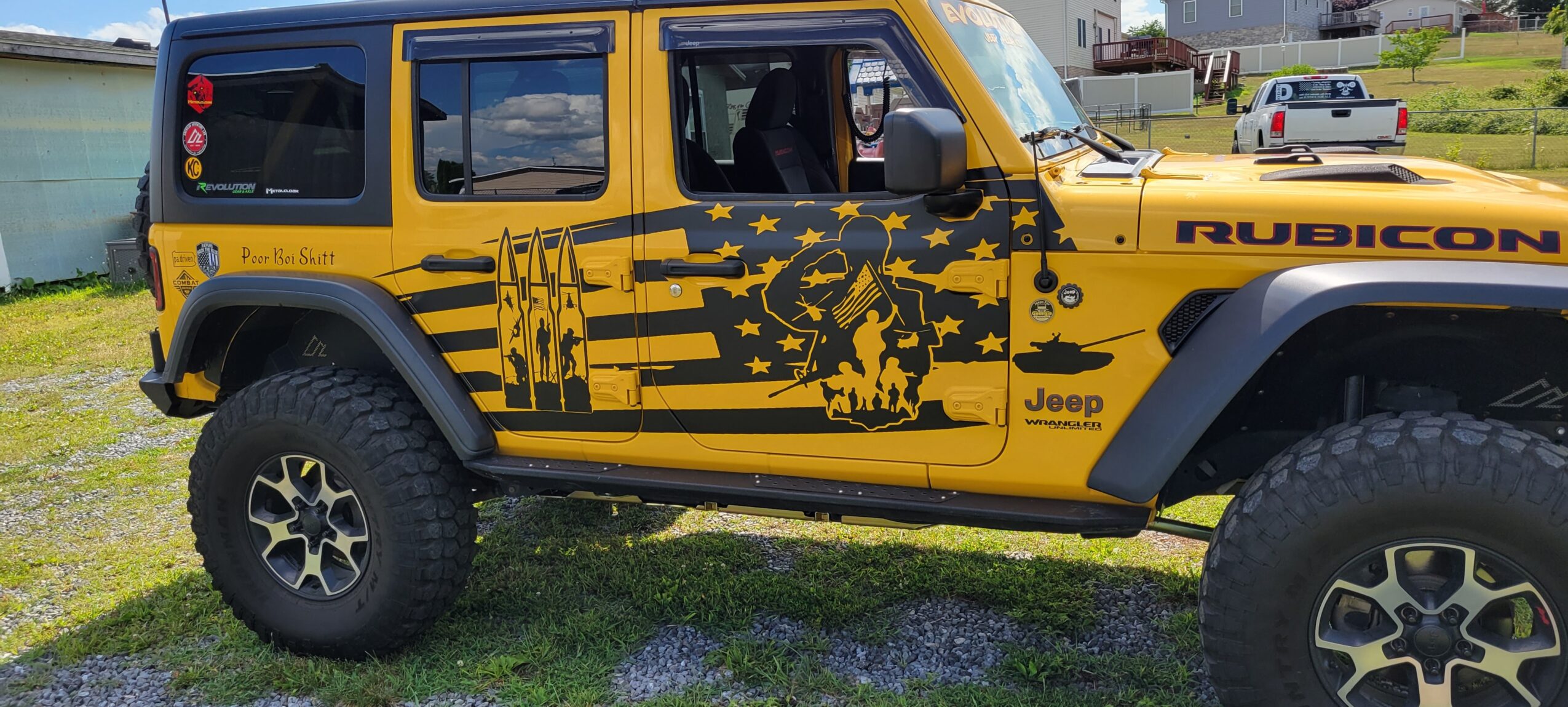 Yellow Jeep Rubicon with black star and stripe design parked on grass, side view, clear sky background.
