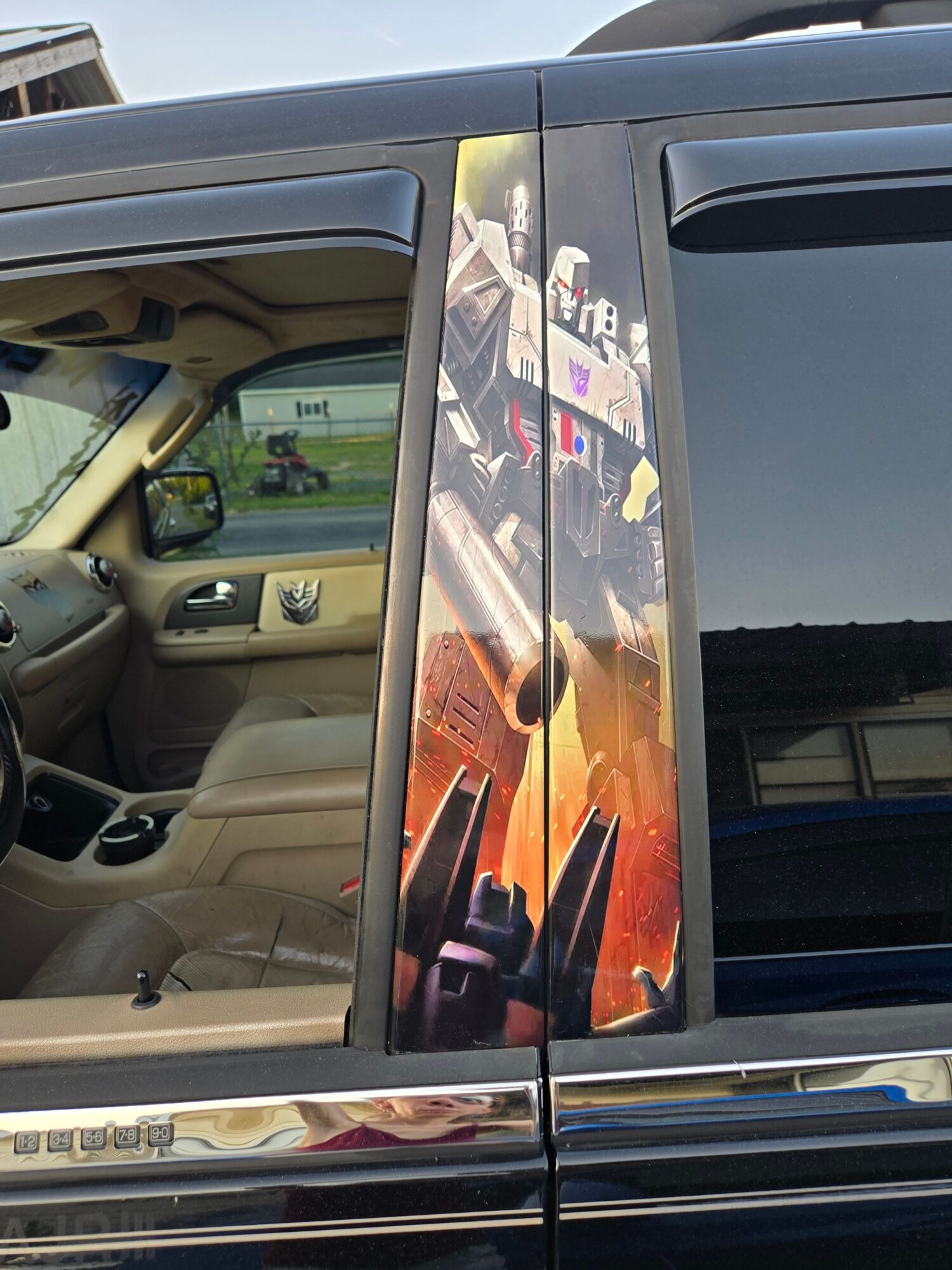 Reflection of a person taking a photo in a shiny surface, with a vehicle interior visible in the background.