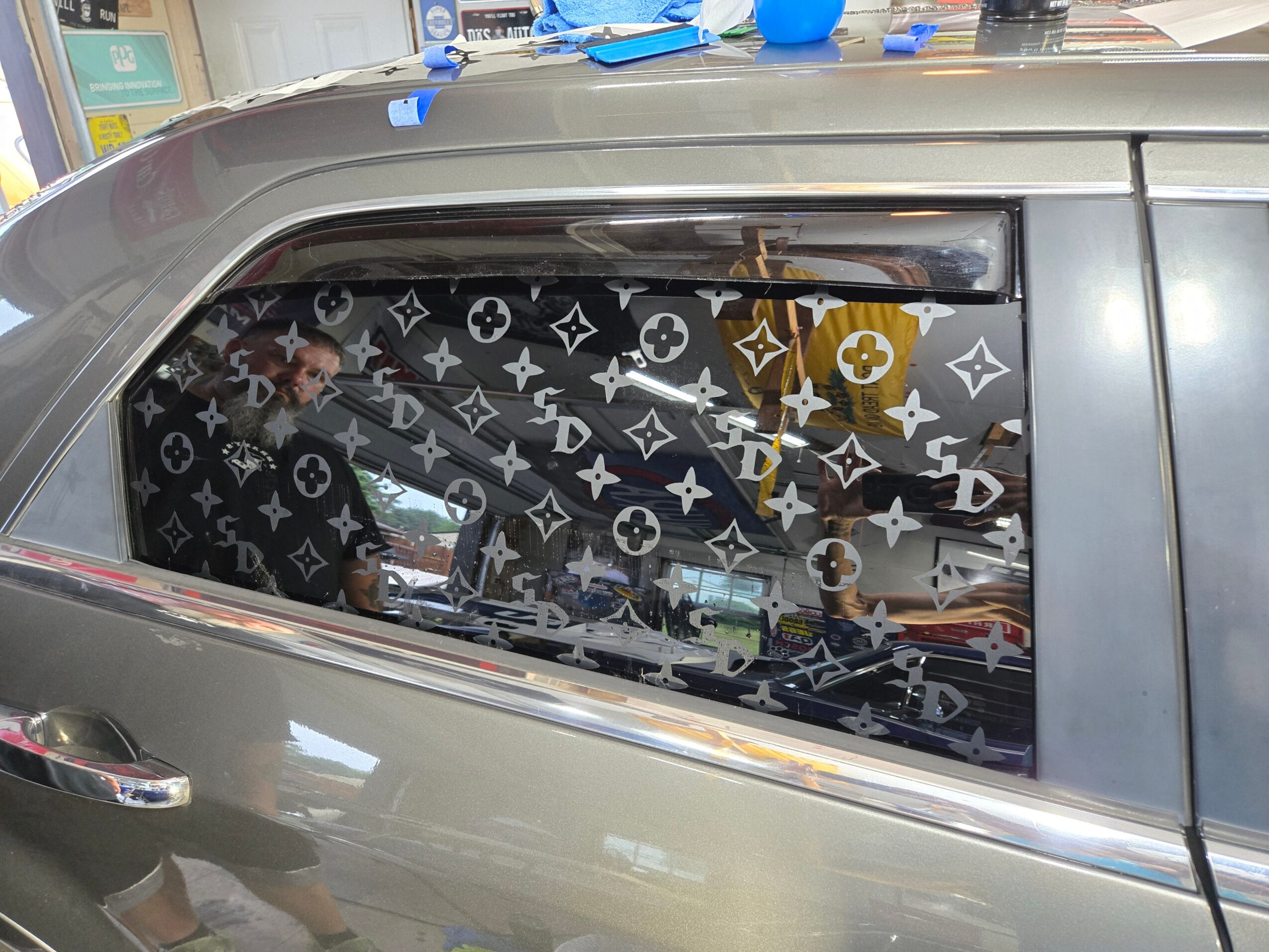 View of a car window with a patterned curtain, showing a person inside and city buildings reflected on the glass.