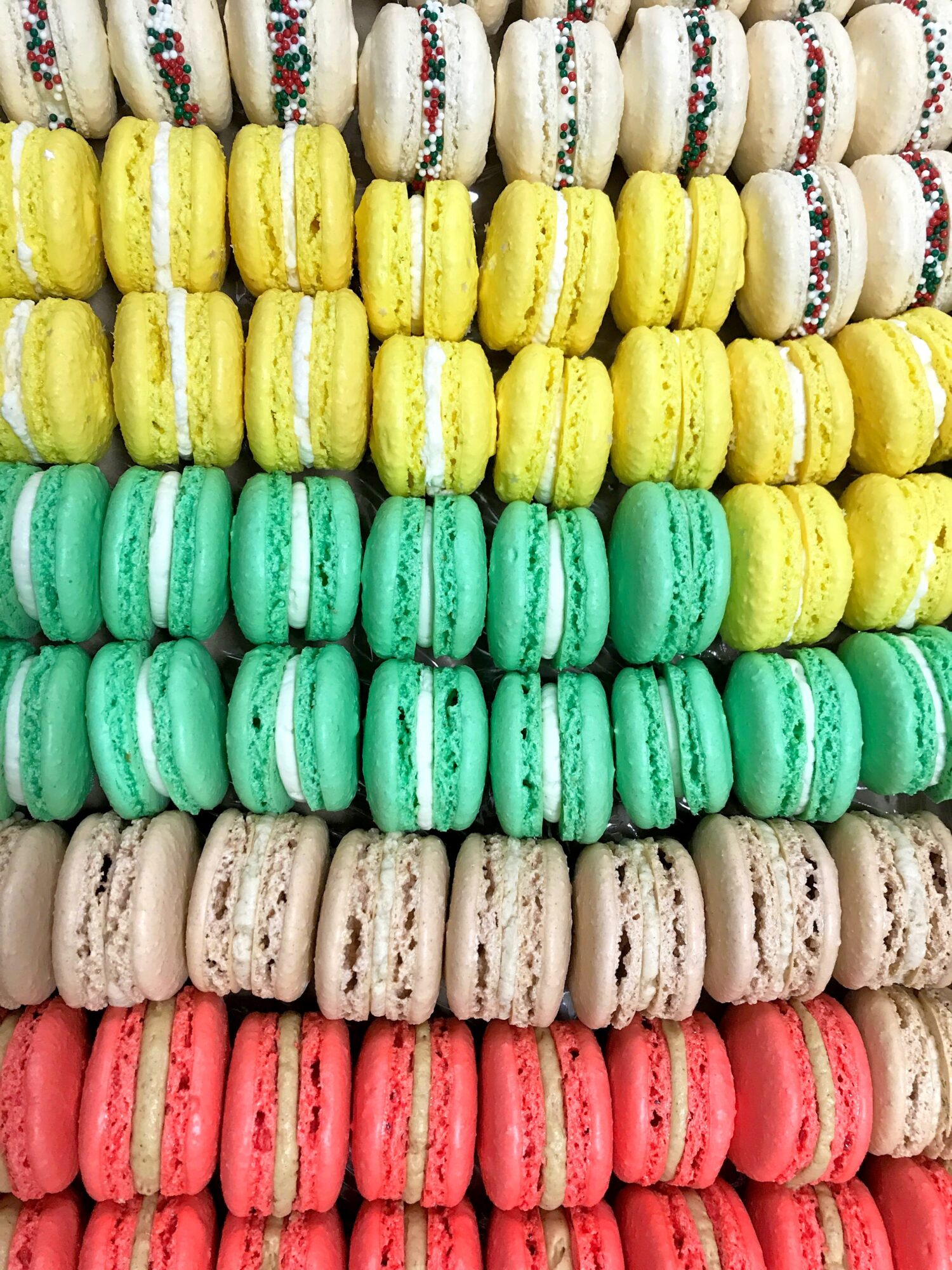 Colorful macarons arranged in rows with white, yellow, green, beige, and pink colors, stacked vertically.
