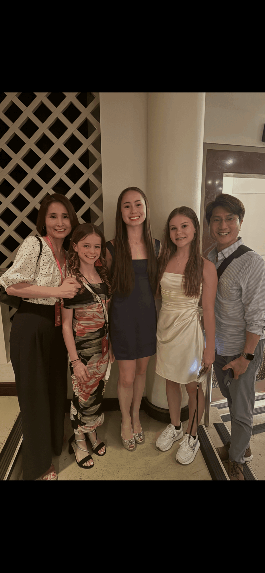 Five people standing together indoors, smiling, with a lattice wall behind them.