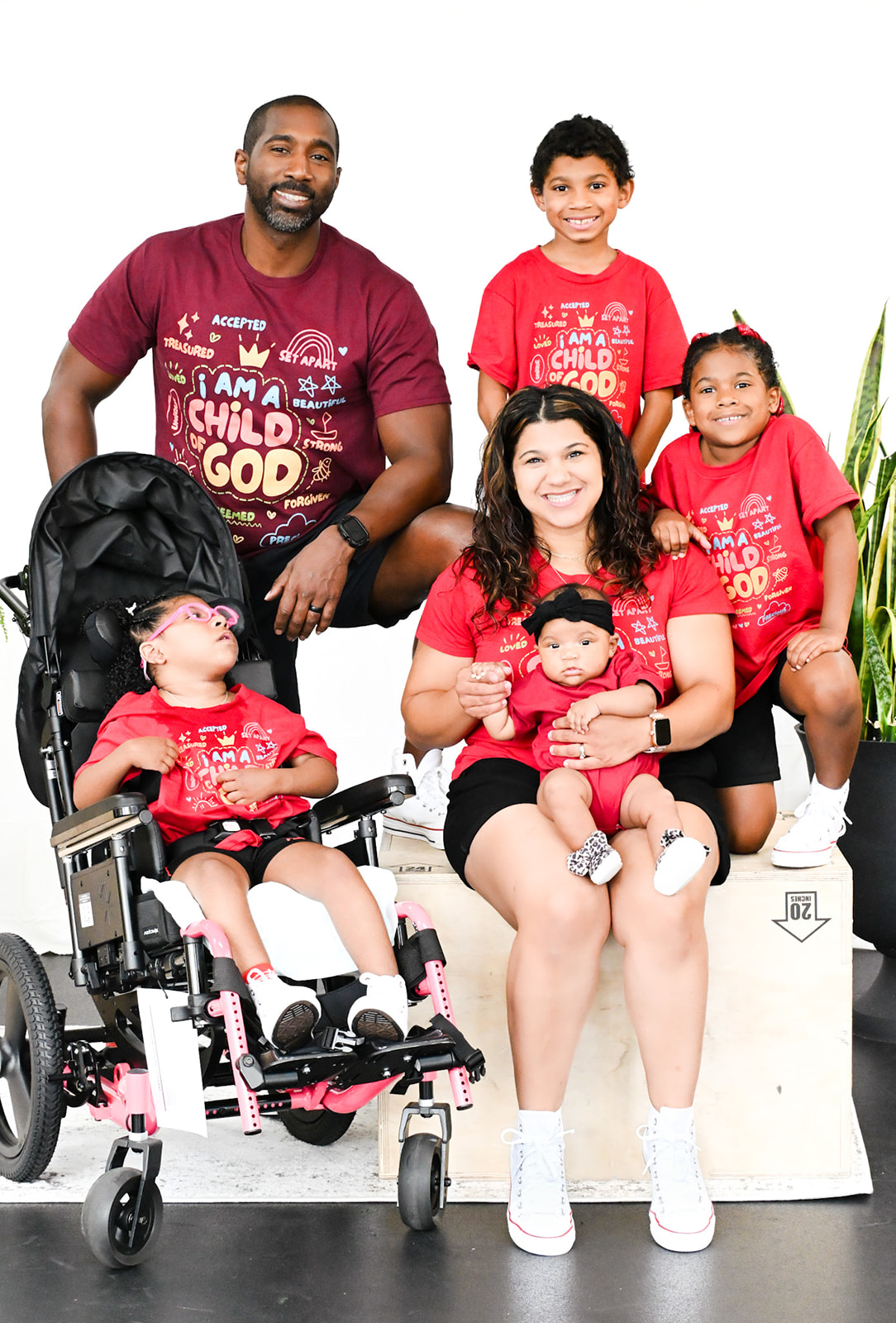 Group of five people, including children and adults, posing together, some sitting and some standing, against a white background.