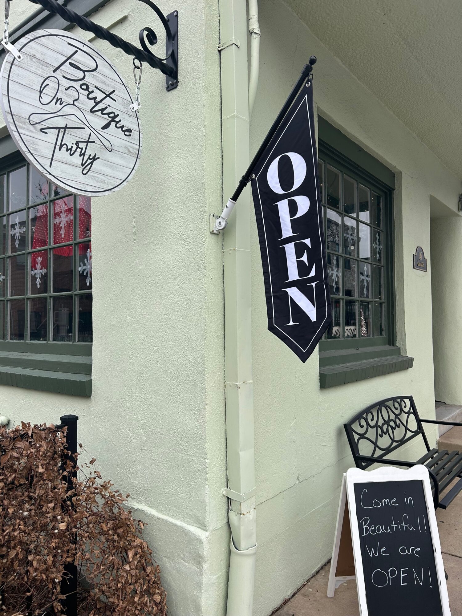 Storefront with a black and white sign, window, and a chalkboard sign outside, with a textured ground surface.
