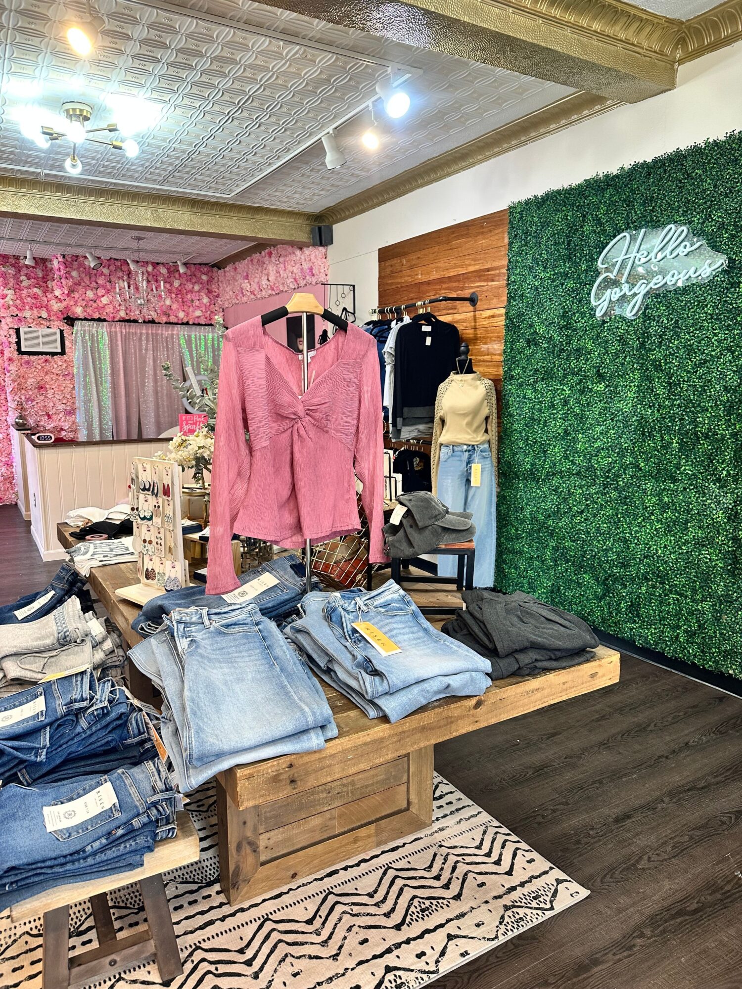 Clothing and bags on a wooden bench in a room with a green wall and patterned rug.