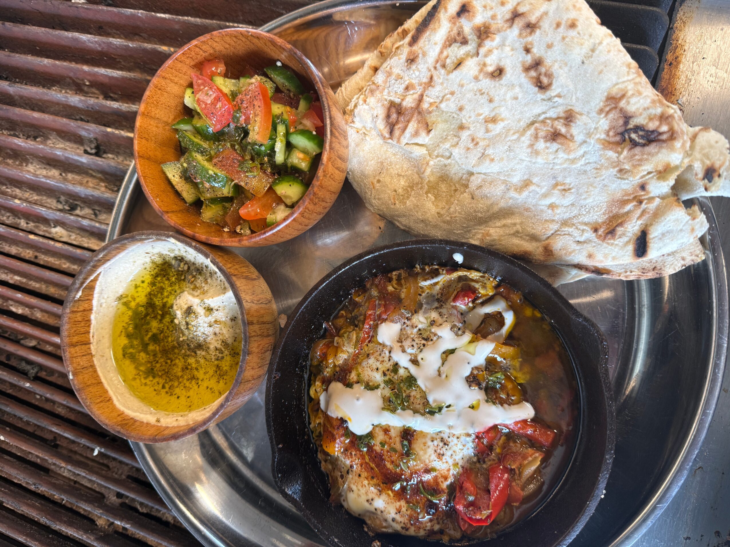 Plate with naan bread, bowl of mixed vegetables, bowl of oil, and a dish with sauce and toppings on a metal tray.