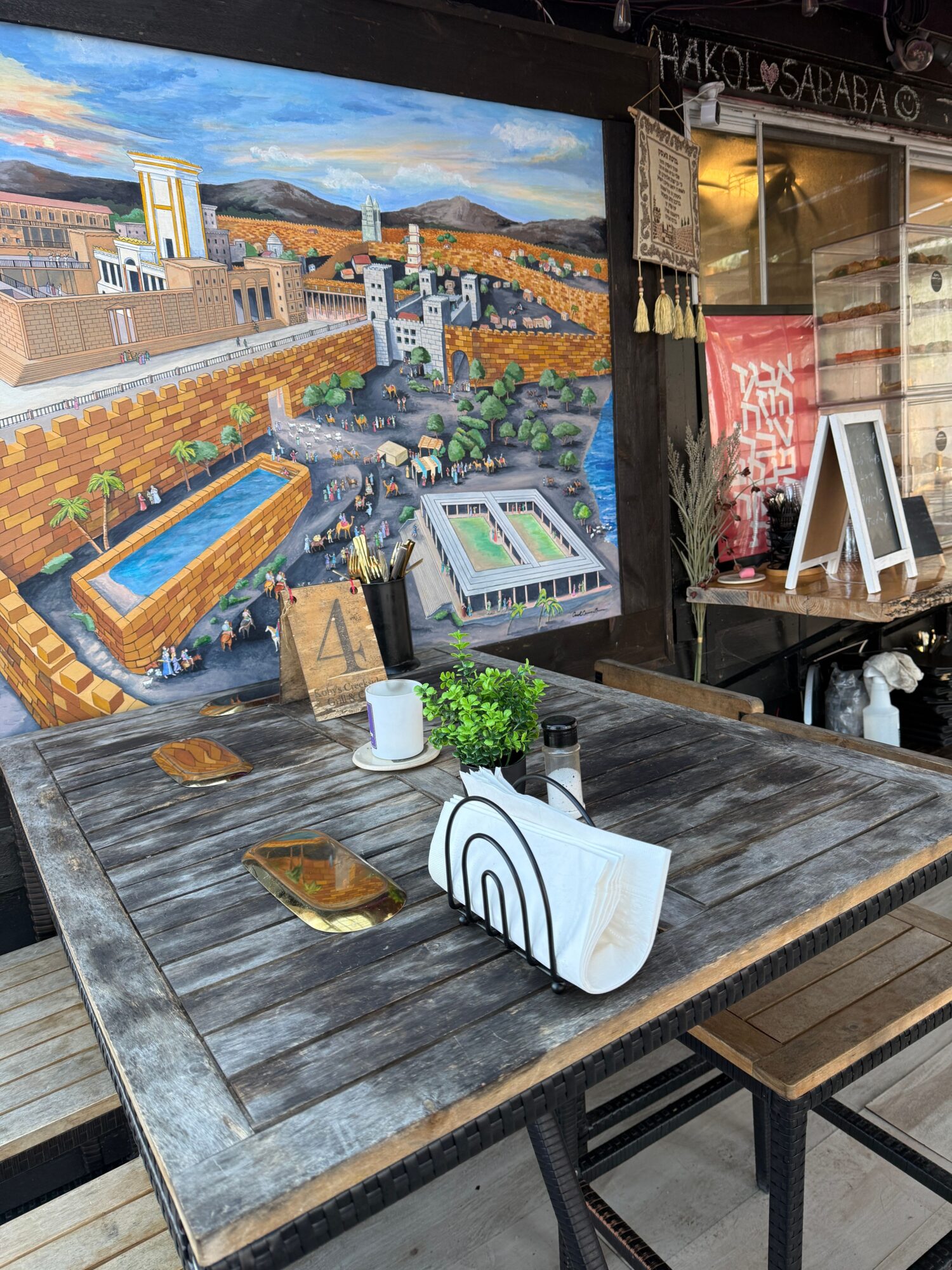 Wooden table with a small plant, tissue box, and decorative items, set in a cafe or restaurant with chairs around.