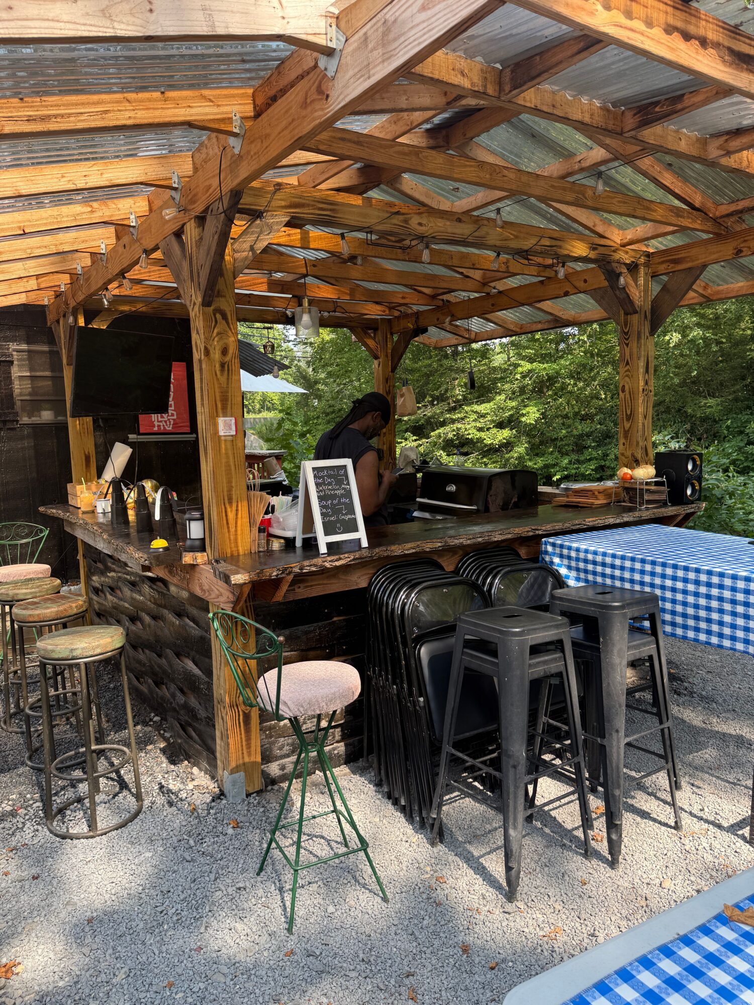 Outdoor bar area with stacked black chairs, a person working on a computer, and a wooden pergola structure.