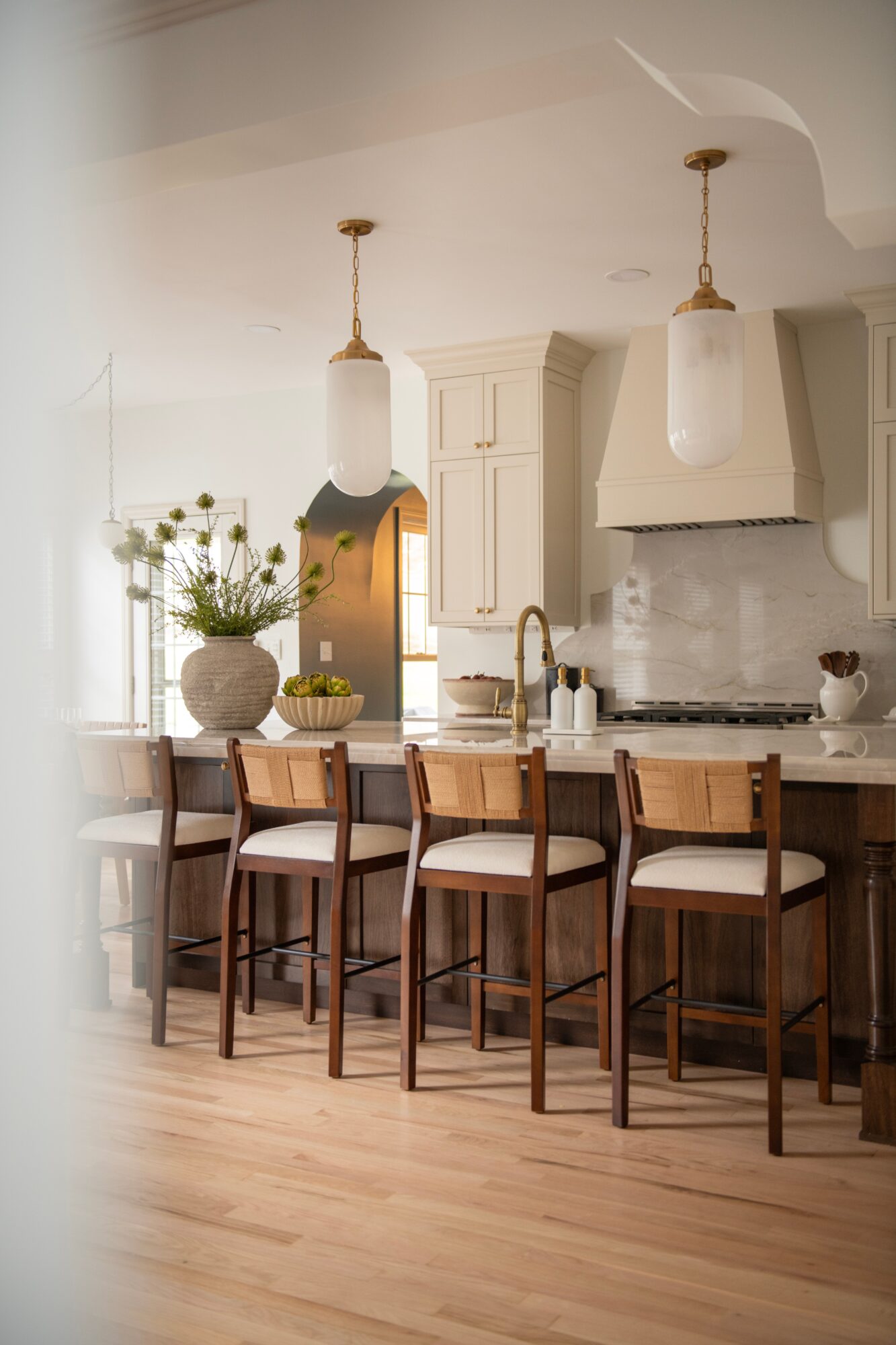 Kitchen with white cabinets, pendant lights, a marble backsplash, and a wooden island with four chairs, bright and airy.